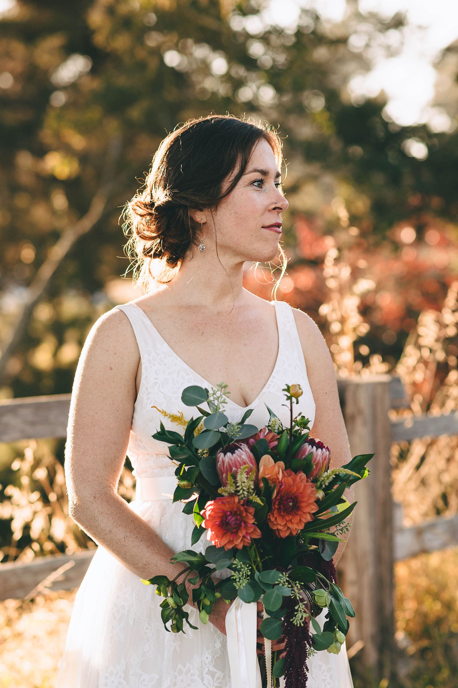 Beautiful bride in a golden grassy field with bouquet of red and orange flowers.