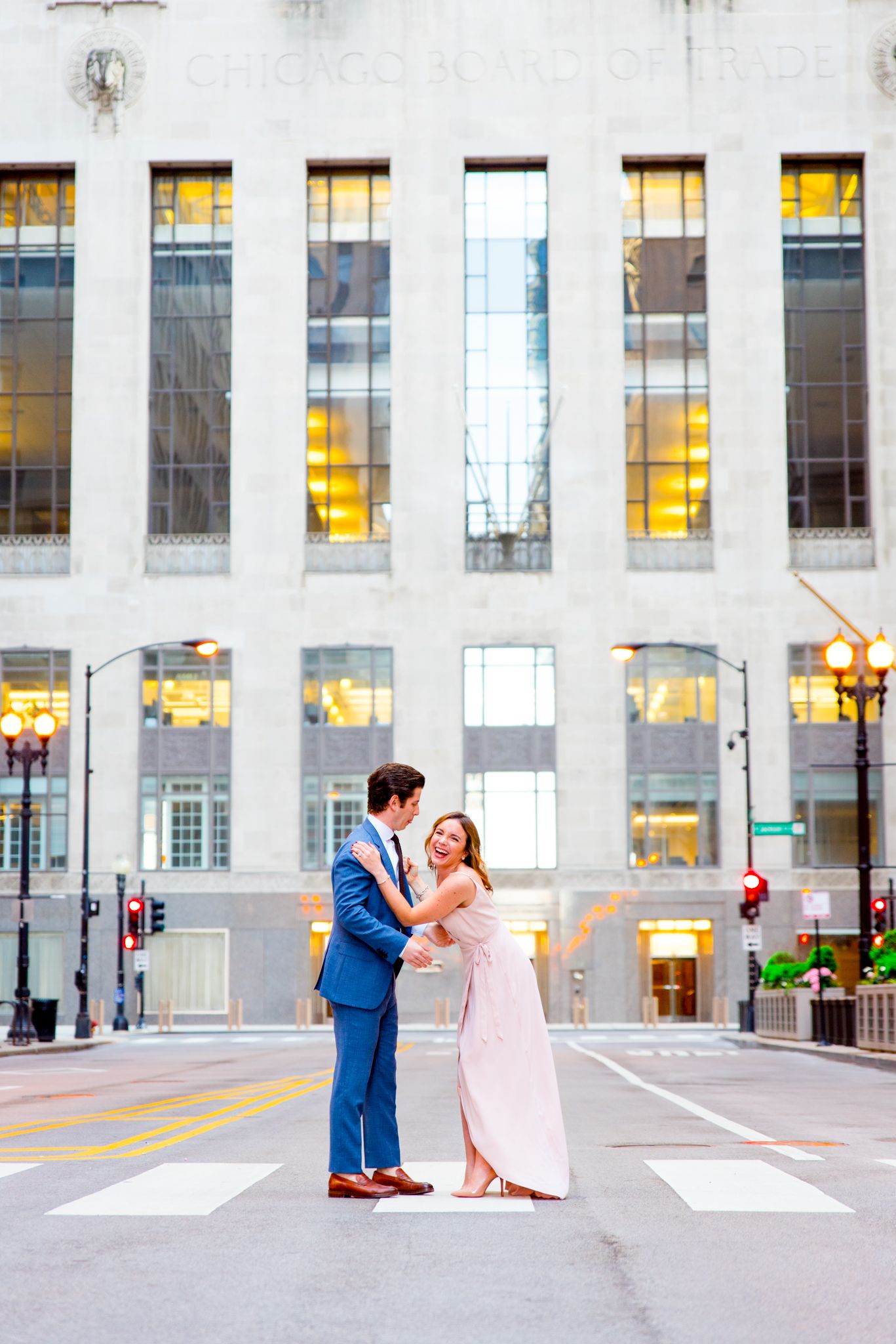 young couple laughs in front of Chicago Board of Trade for sunset engagement pictures in Chicago