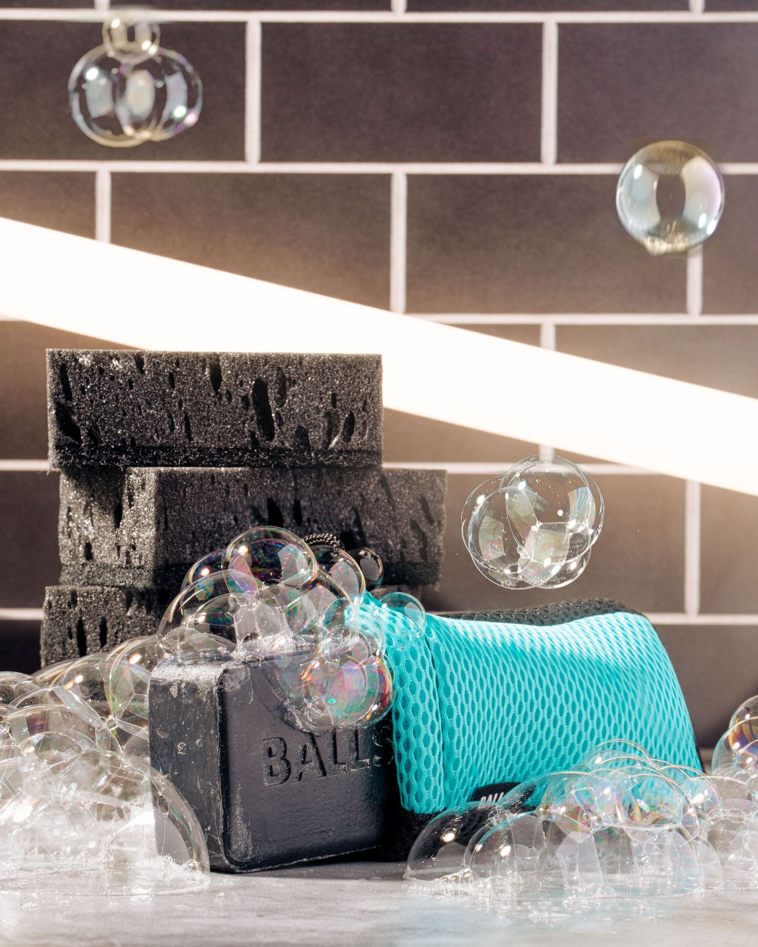 Black soap bars with turquoise washcloth and bubbles against dark tile background.