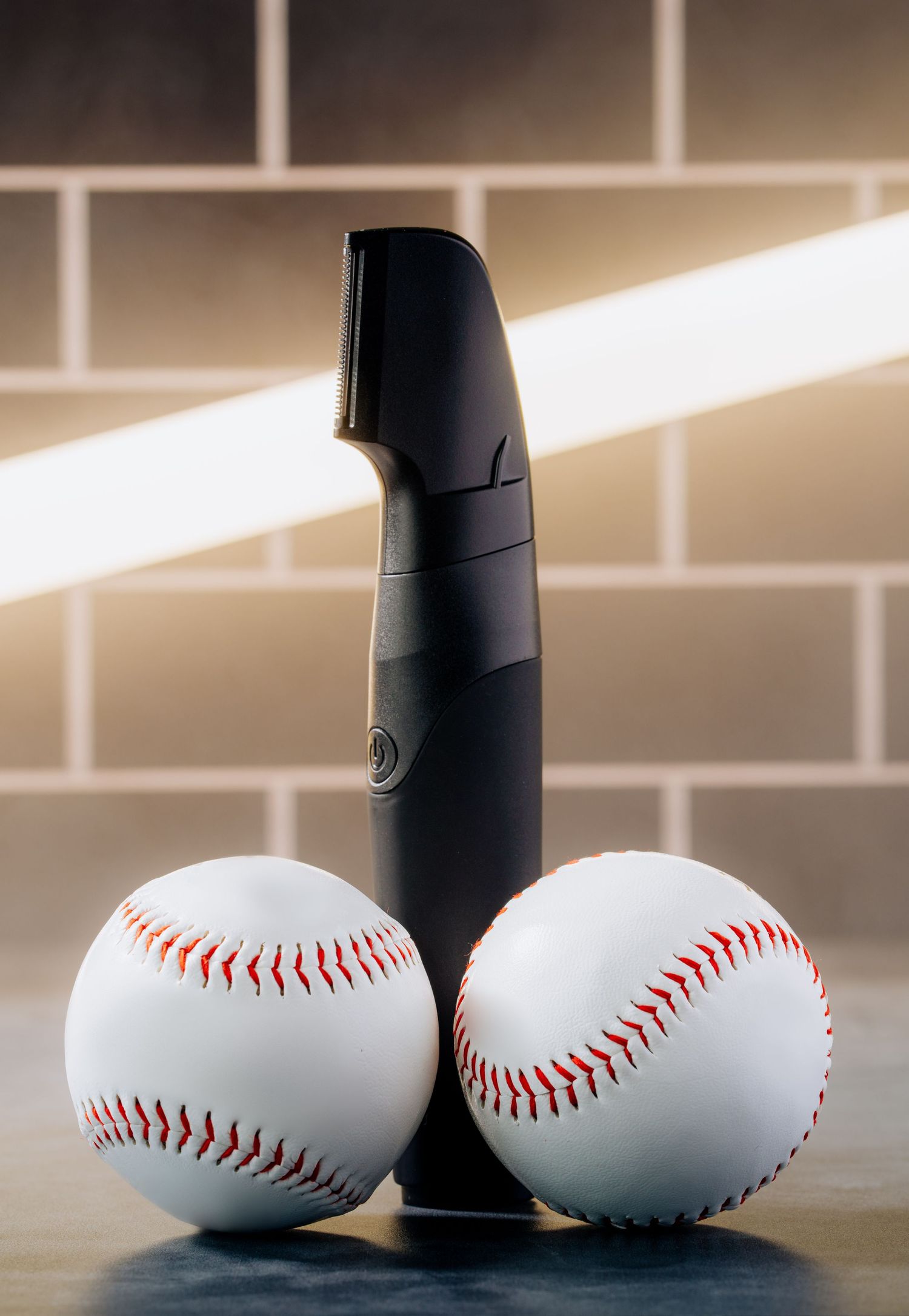 Black grooming device positioned between two white baseballs against tiled wall.