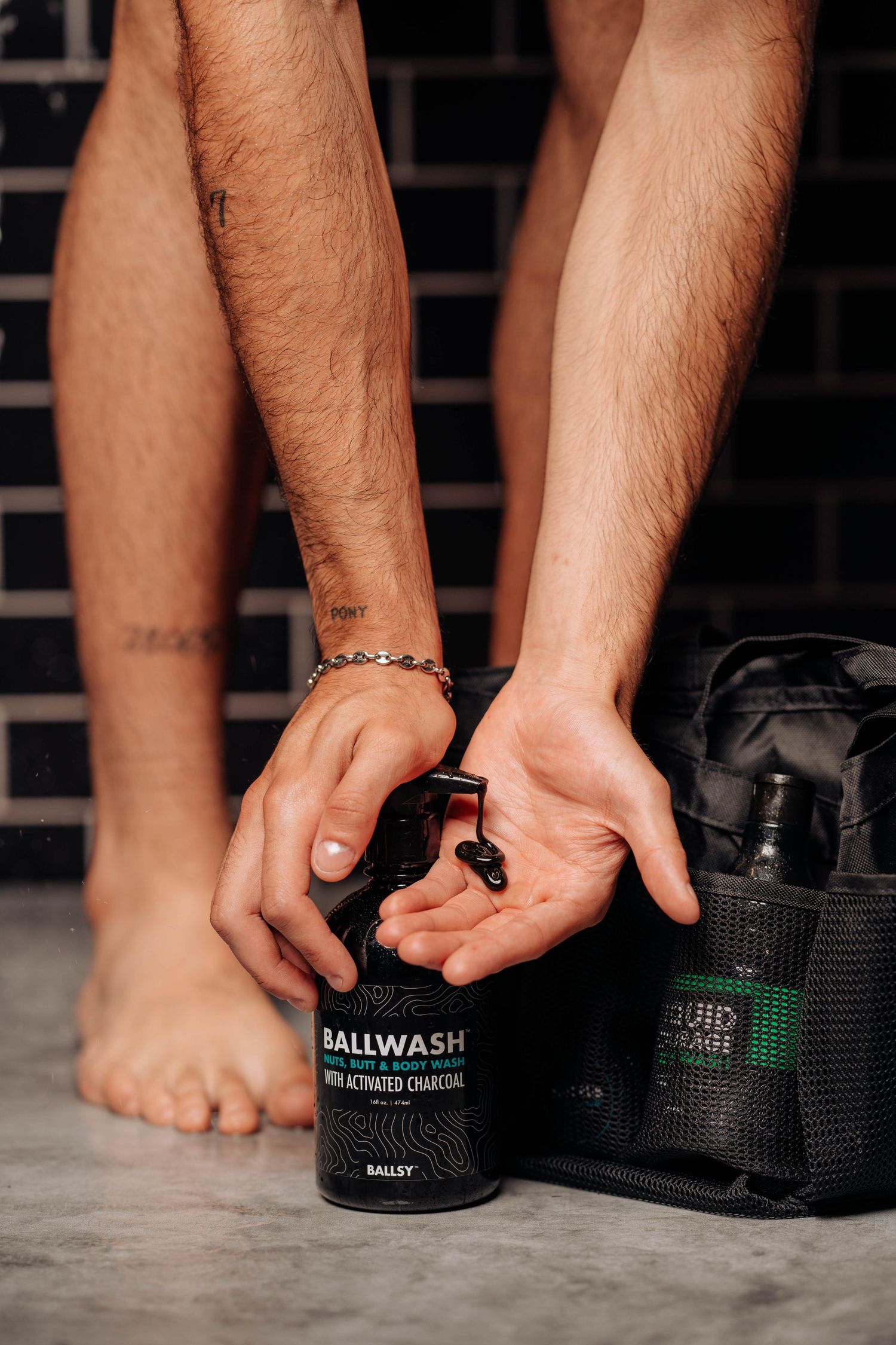 Black Ballwash product bottle being held near a gym bag on dark floor.