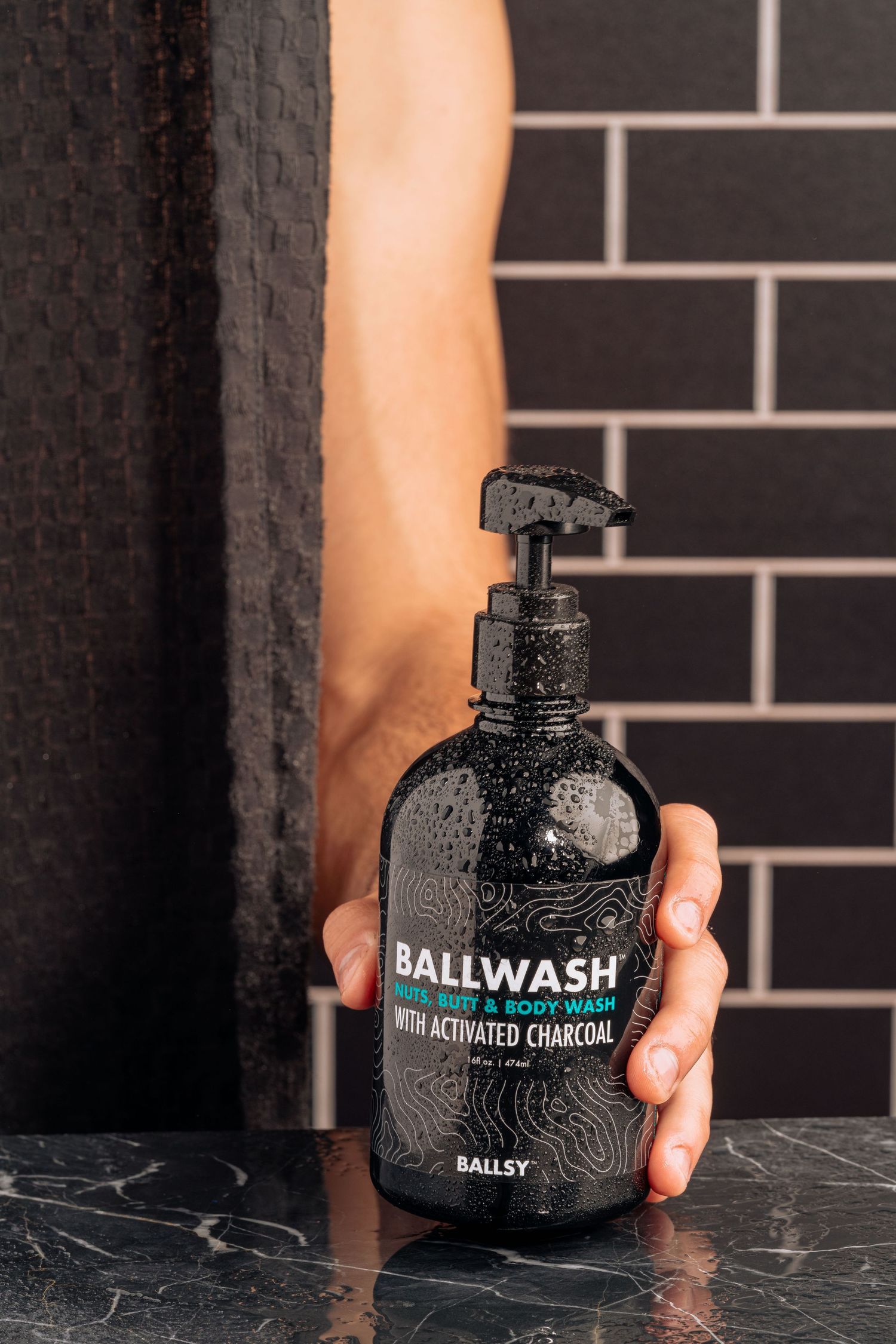 Black Ballwash charcoal body wash bottle displayed against black tile wall.