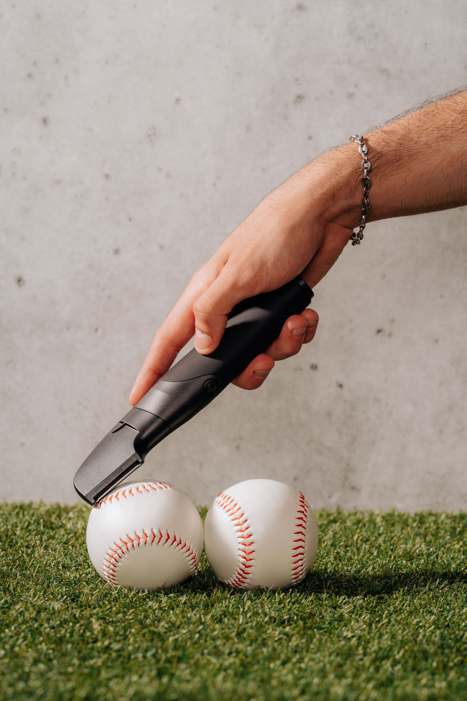Hand holding grooming product over two baseballs on artificial turf.