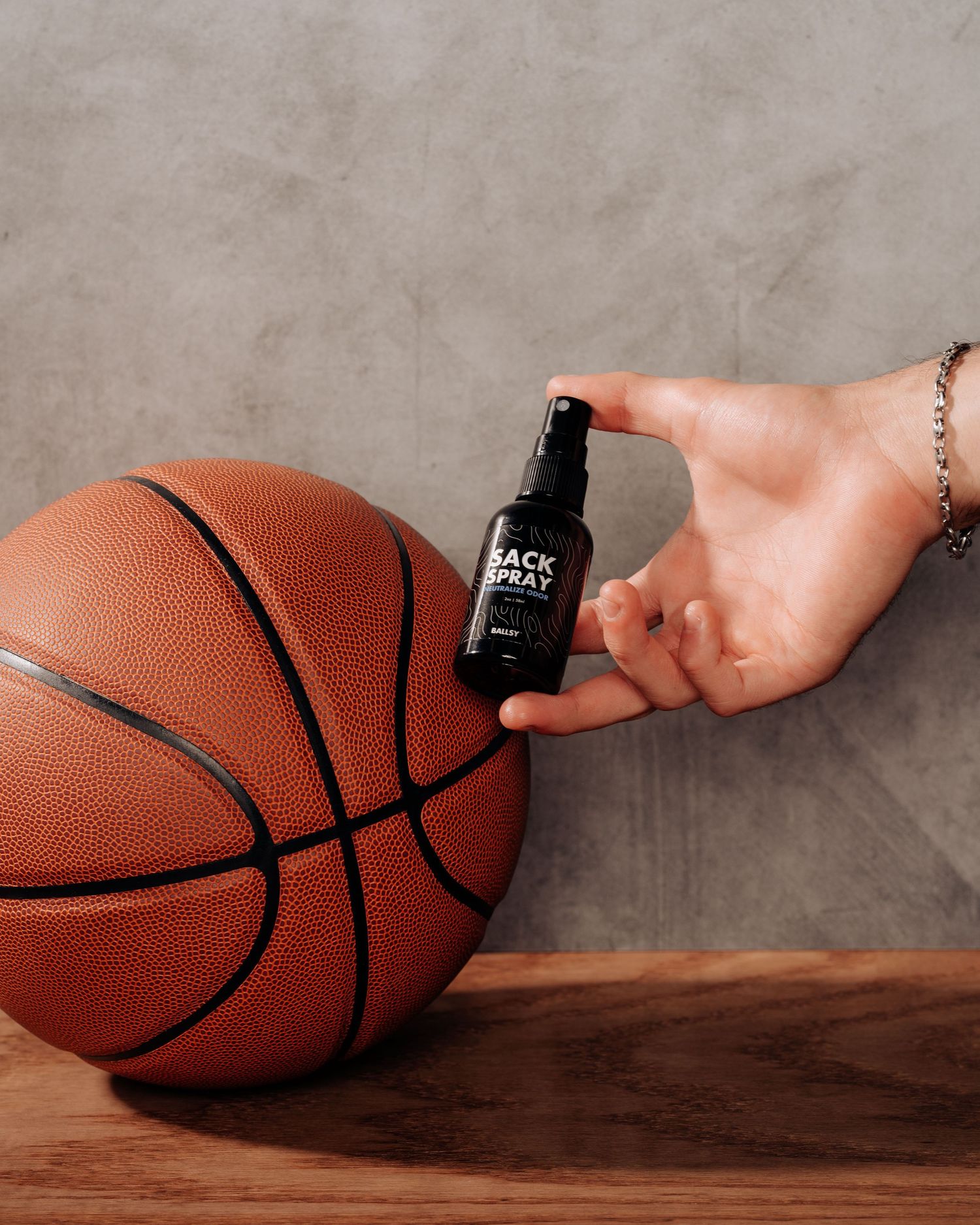 Black spray bottle product displayed next to an orange basketball on wooden surface.
