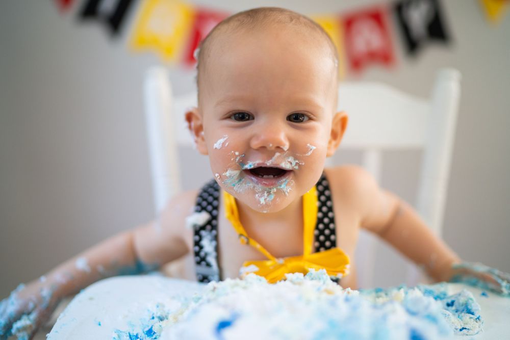 a boy smiling in a highchair eating birthday cake