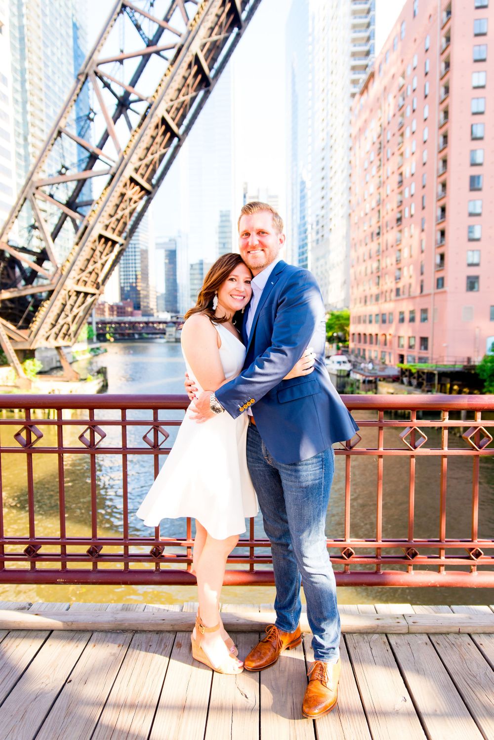man in navy suit and woman in white dress hugging in front of Chicago River for sunset engagement pictures in Chicago