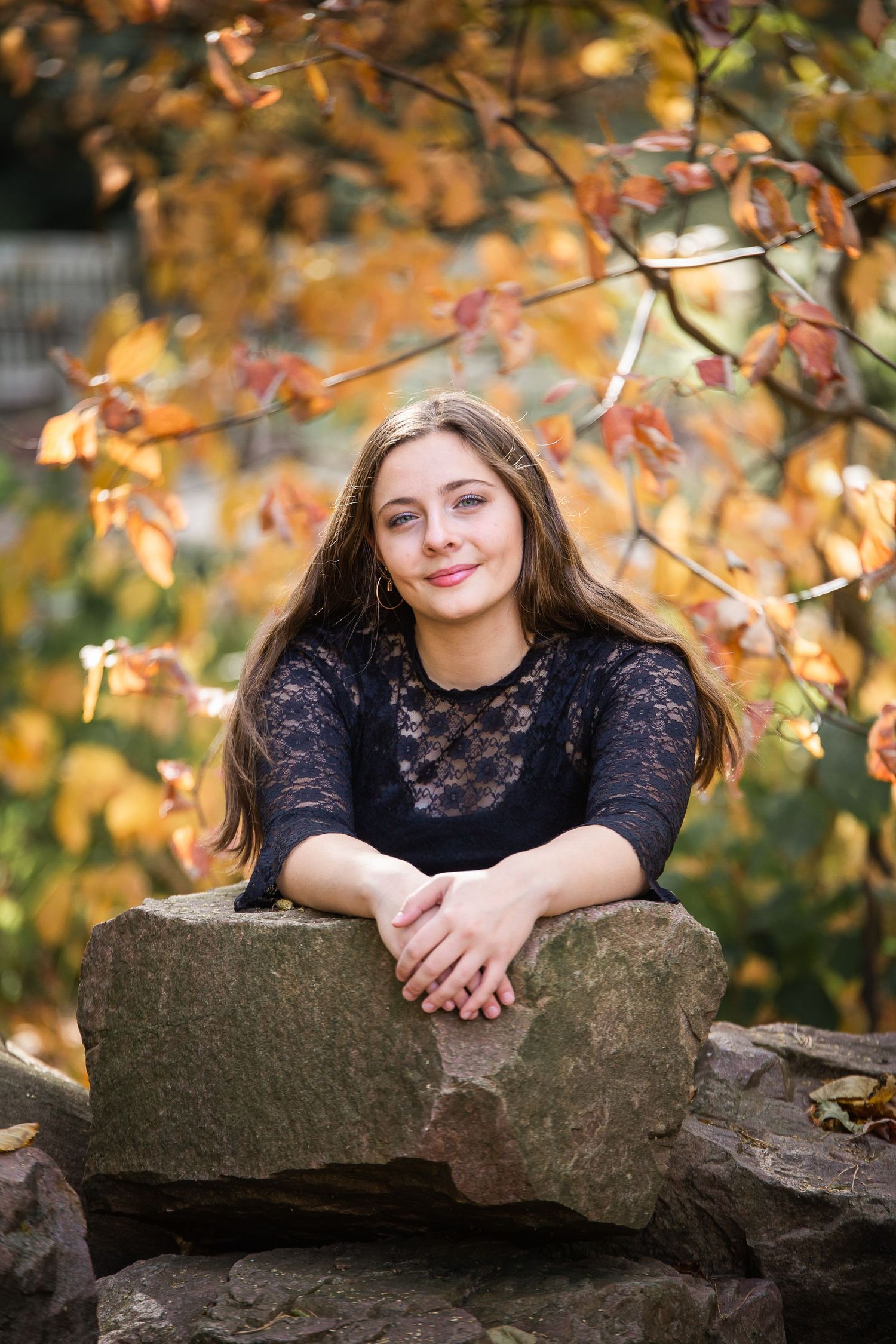 teenage girl leaning on a rock surrounded by fall foliage