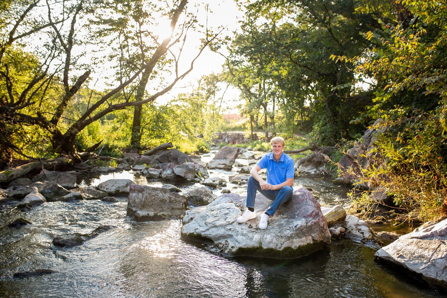 high school senior boy in blue sitting on rocks surrounded by water