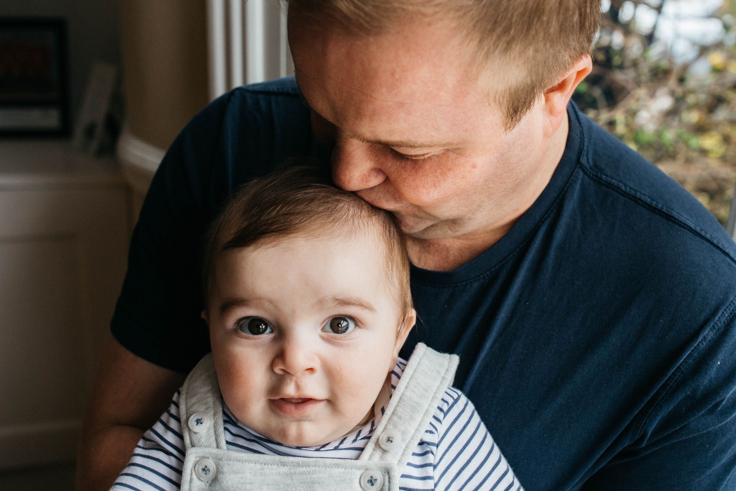 dad in navy t-shirt kissing son on top of head