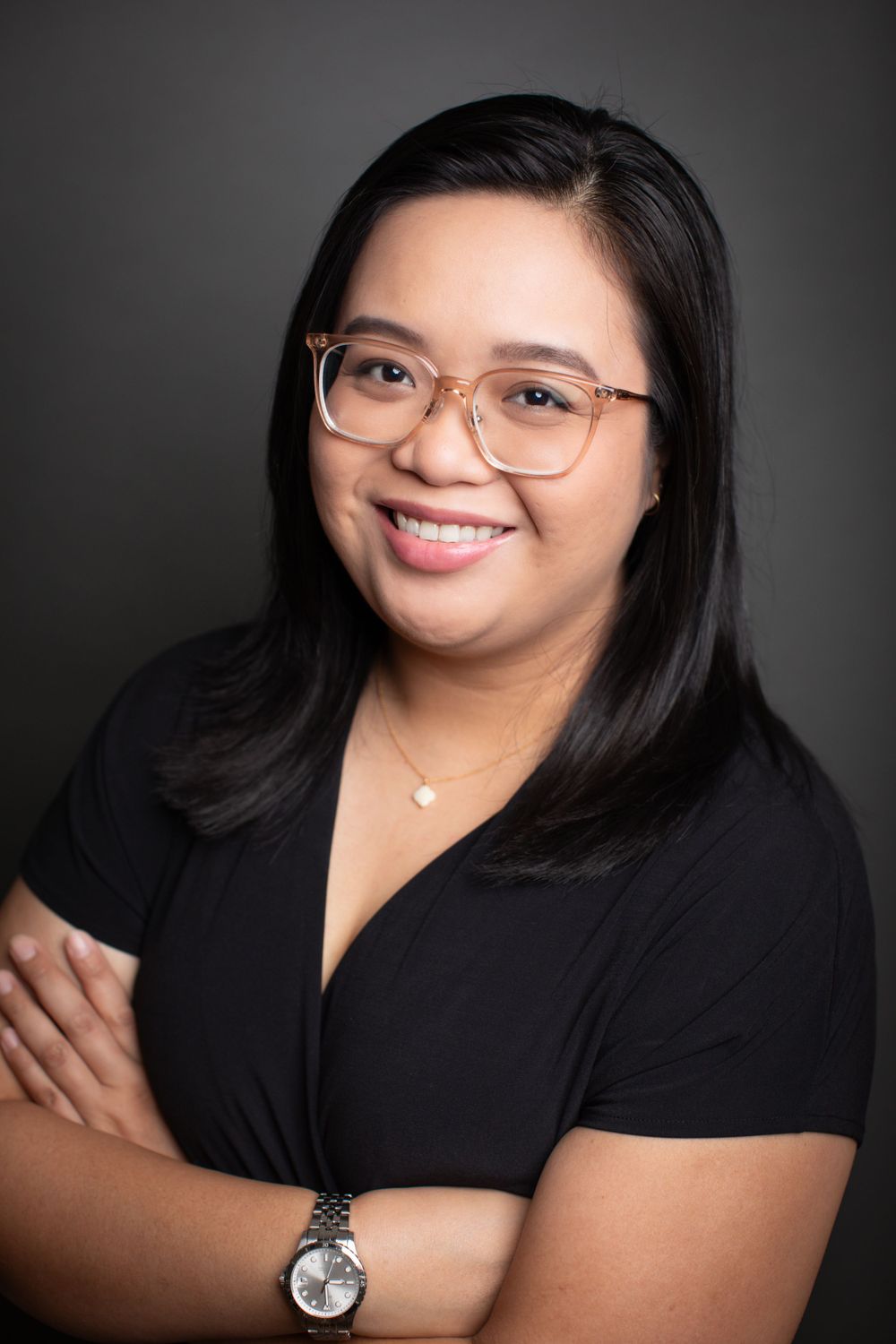 Professional headshot of person wearing glasses and black top against dark background.