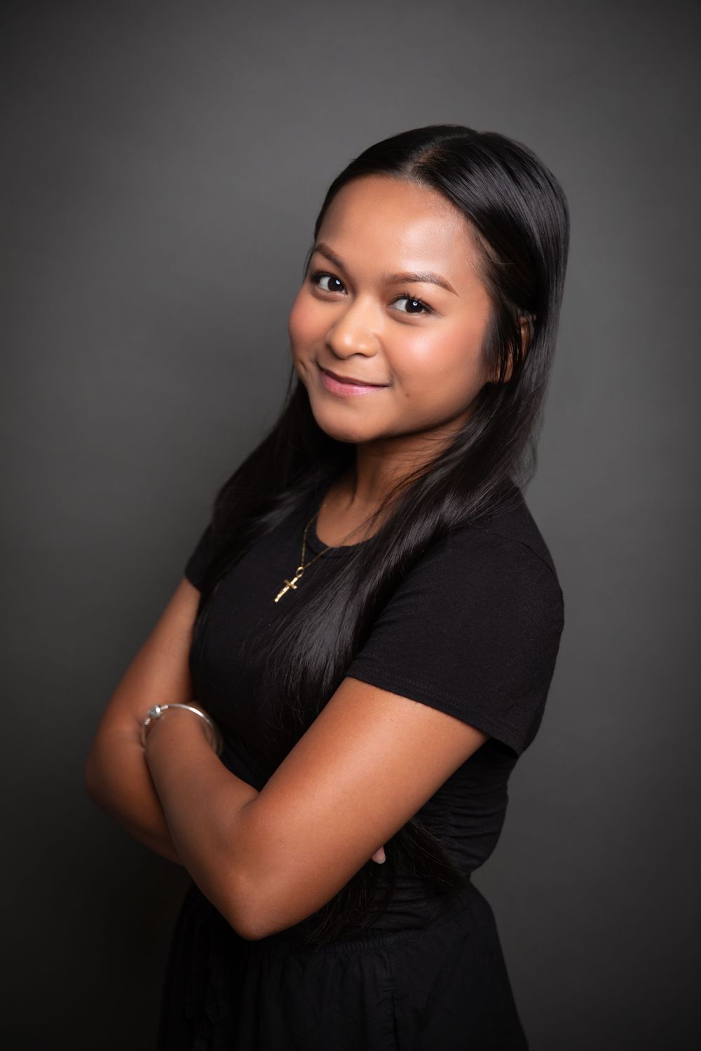 Studio portrait of person in black outfit against dark background with natural smile.