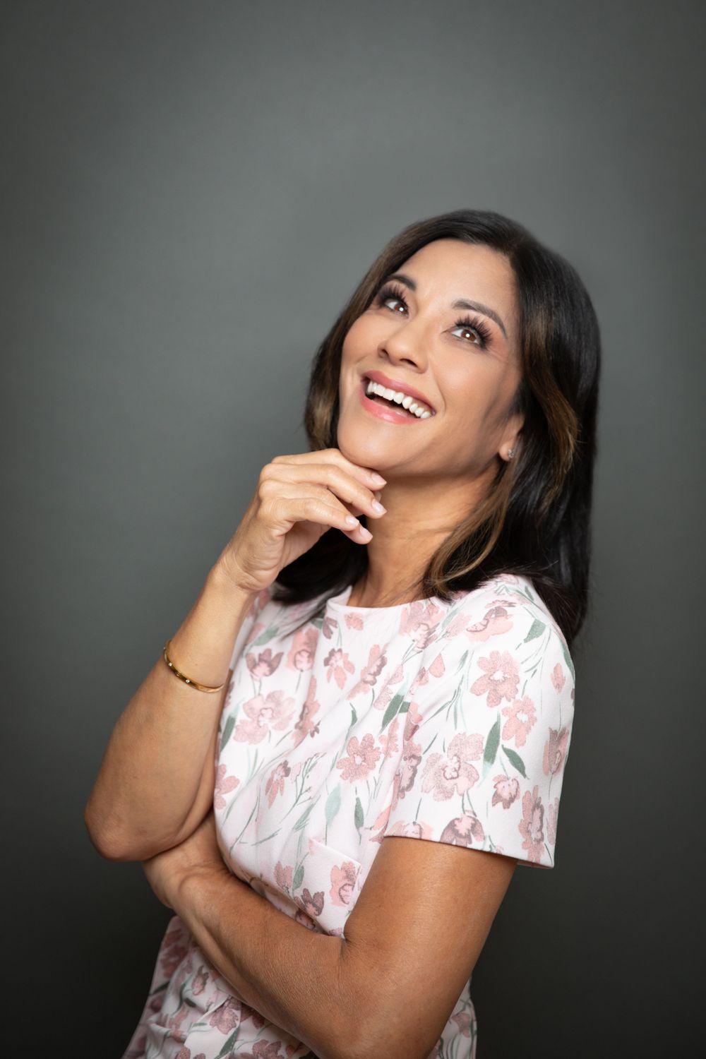 Studio portrait of someone in floral dress looking up thoughtfully against gray background.