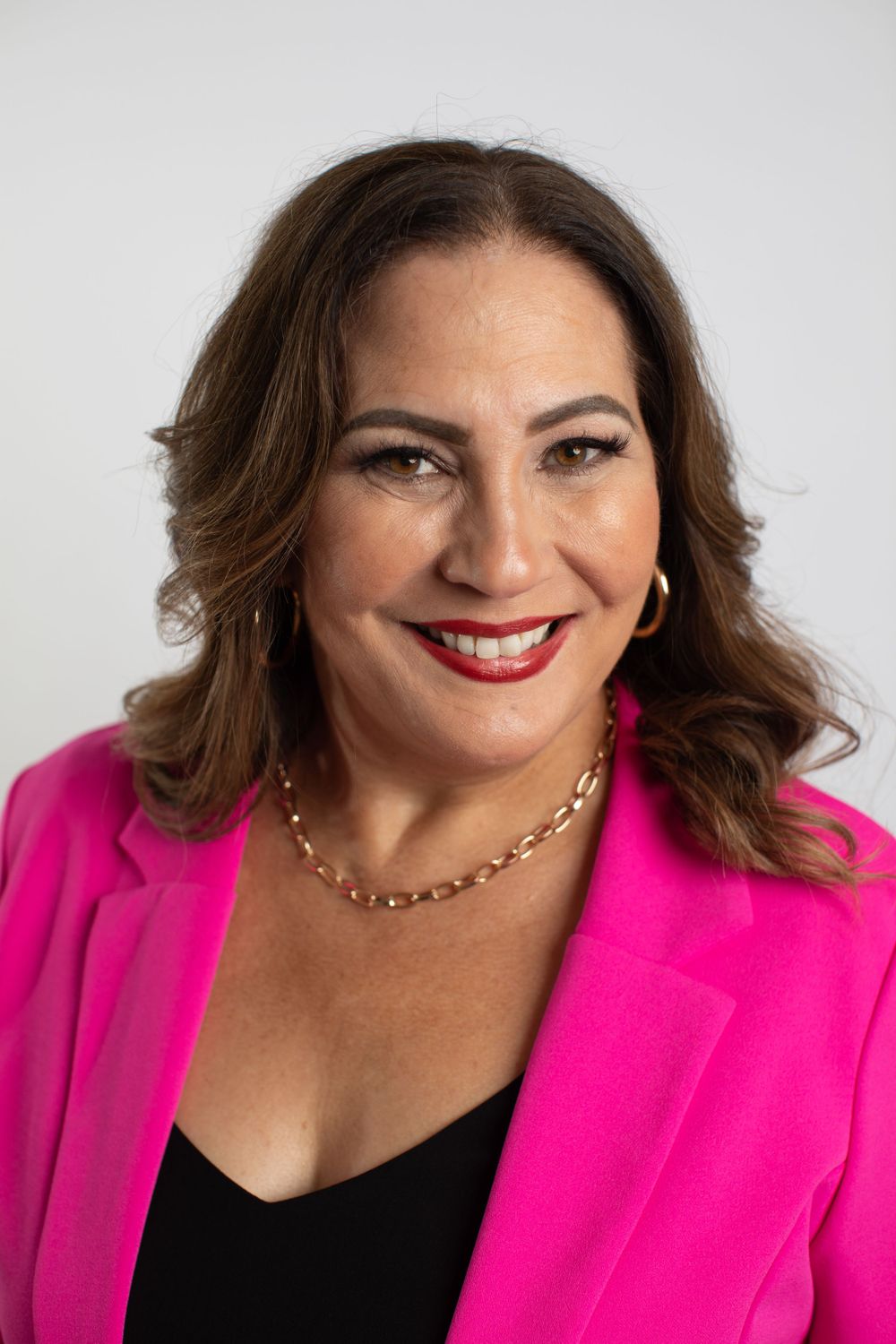 Professional headshot of woman in hot pink blazer and black top against white background.