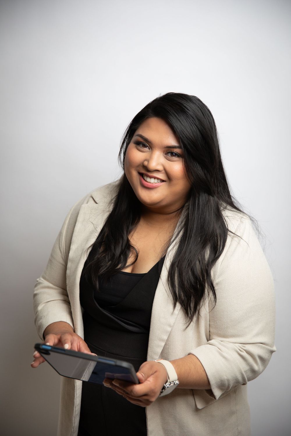 Professional headshot of person in business attire holding a tablet device with a warm smile.