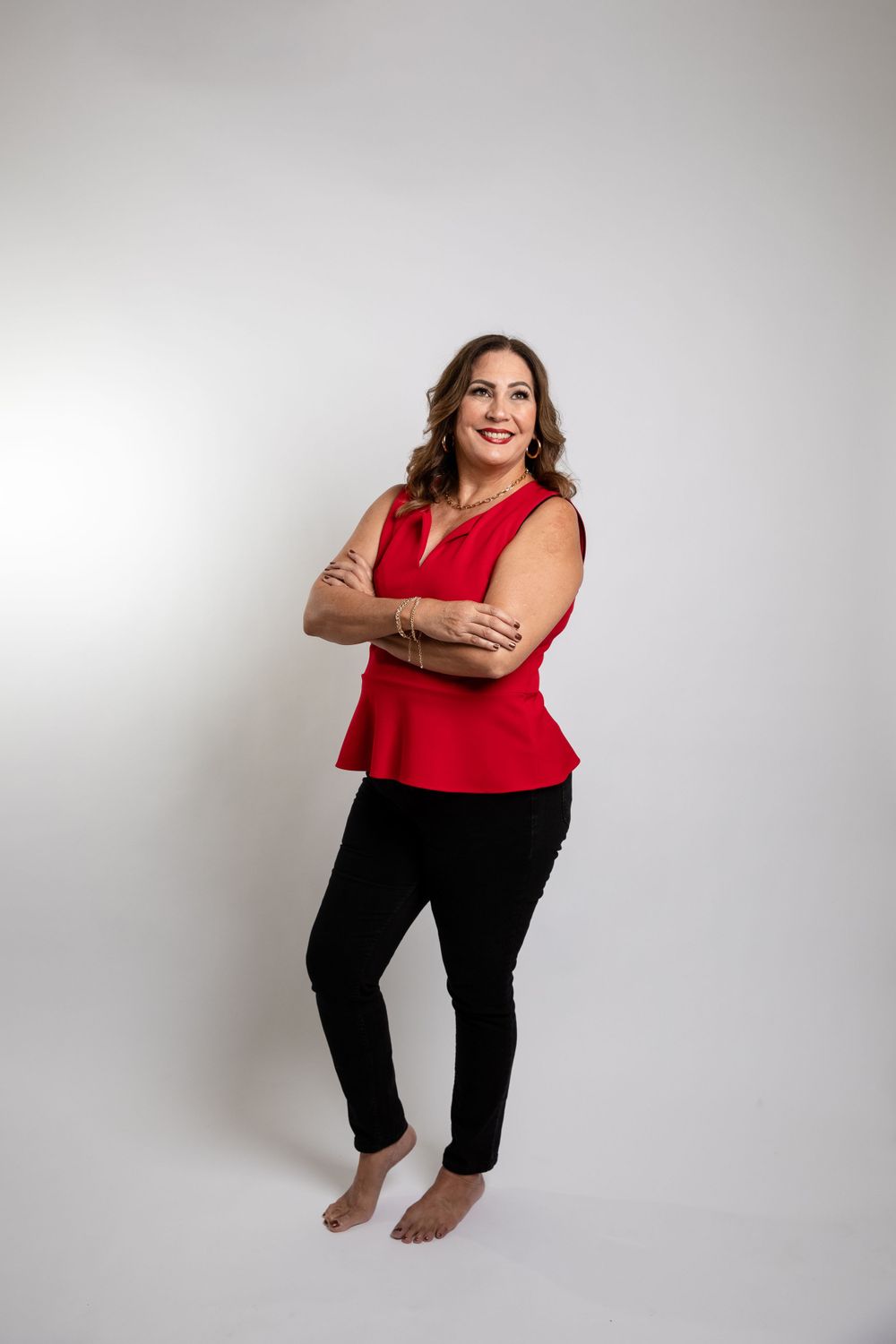 Woman in red sleeveless top and black pants poses confidently against white backdrop.