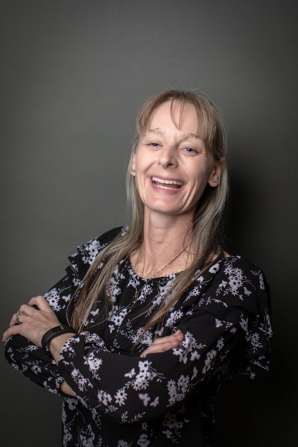 Professional portrait of person with long blonde hair wearing a floral print top against dark background.