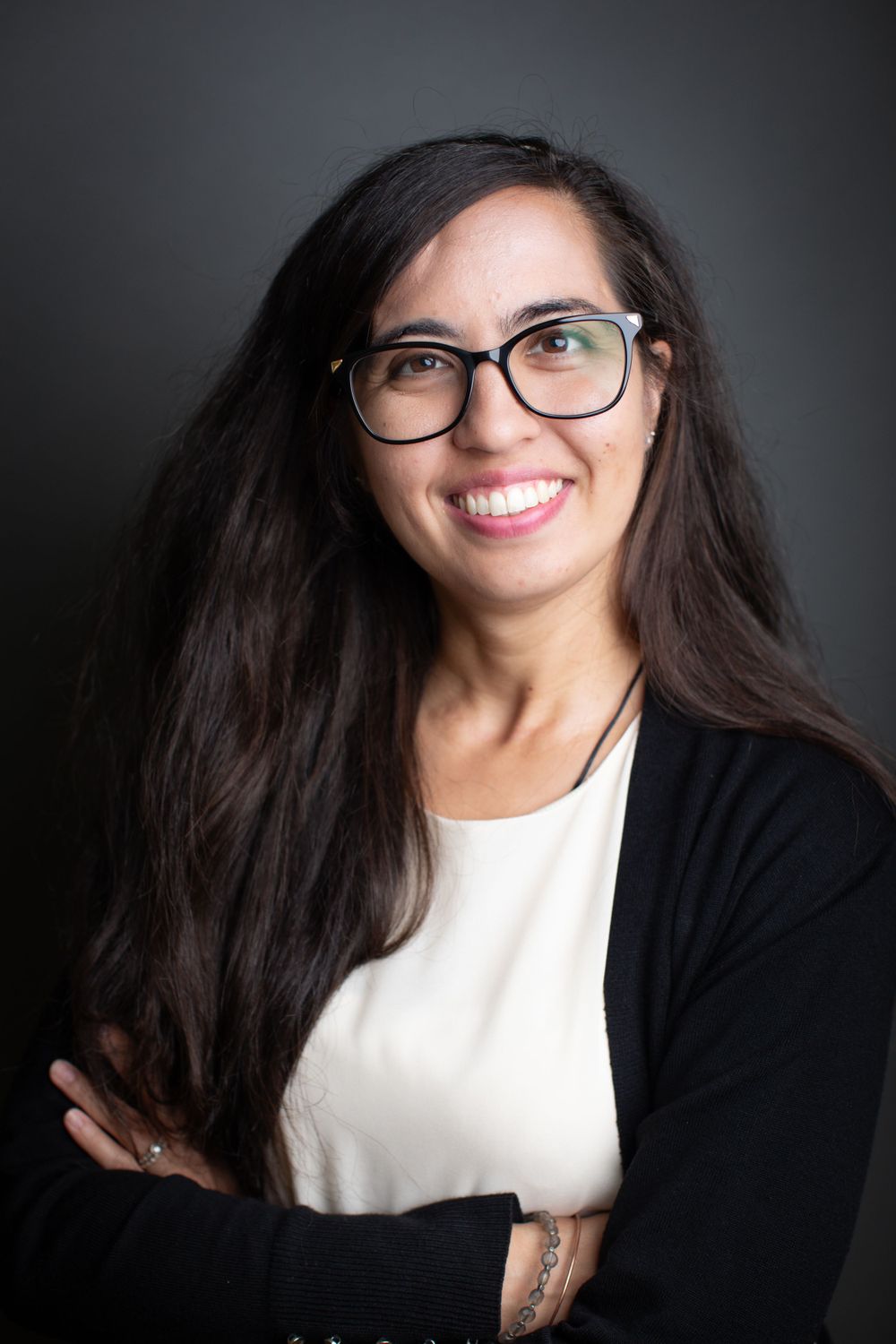 Professional headshot of person wearing glasses and black cardigan against dark background.