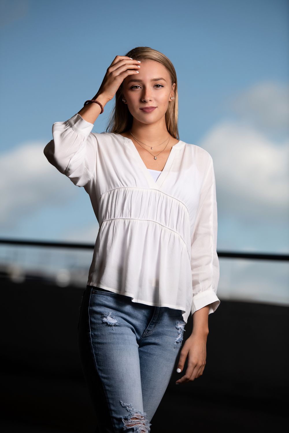 Senior session with a girl in white top and torn blue jeans atop a parking garage, urban setting