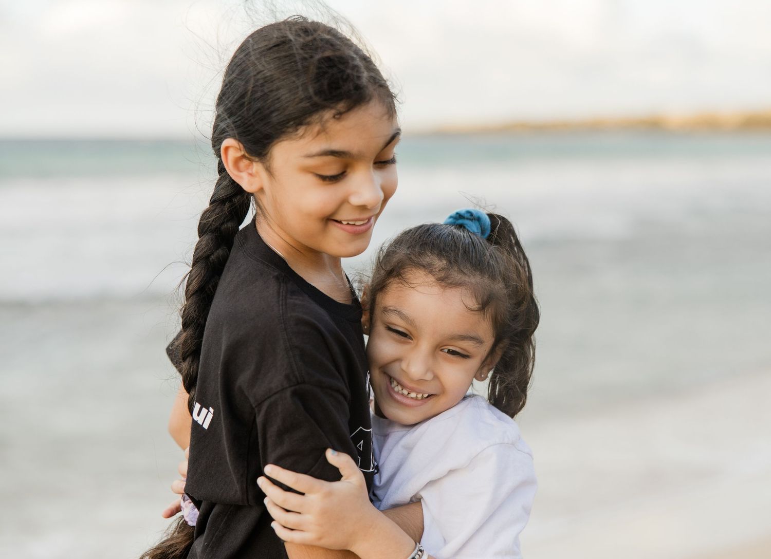 Maui family photographer - two sisters hug each other during photo session .