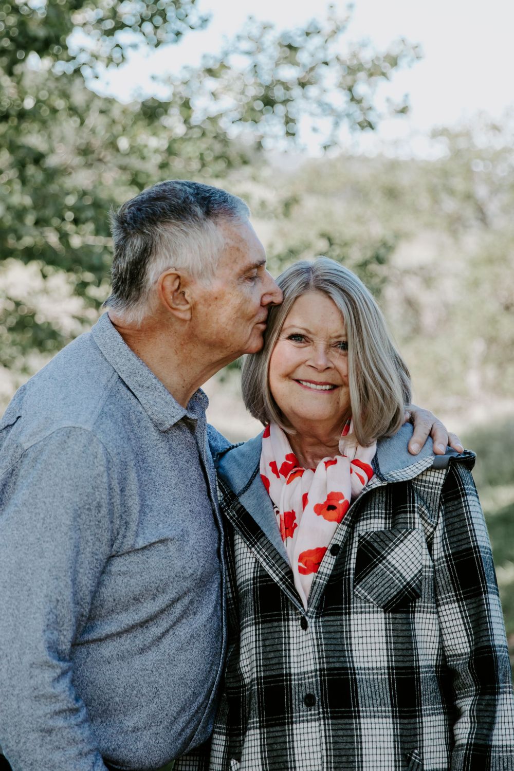 A tender moment between a couple wearing winter attire outdoors in natural lighting.
