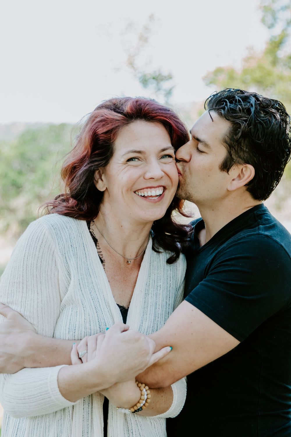 A romantic candid moment between a couple embracing and laughing in natural lighting.