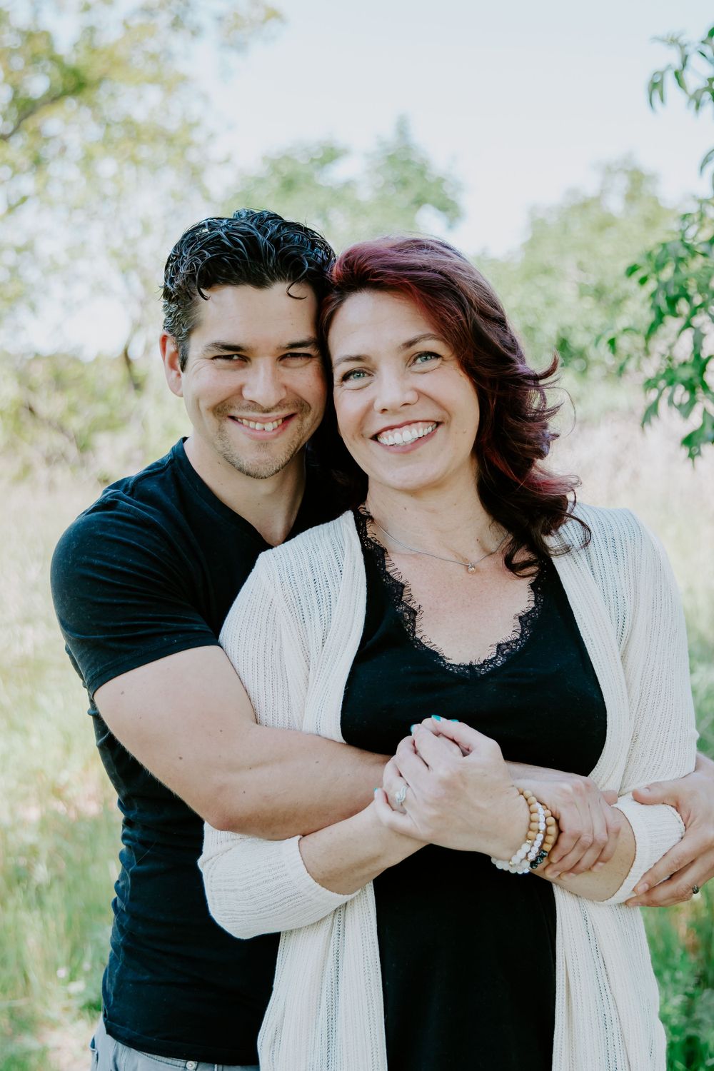A couple in black and white clothing embracing and smiling in an outdoor setting.