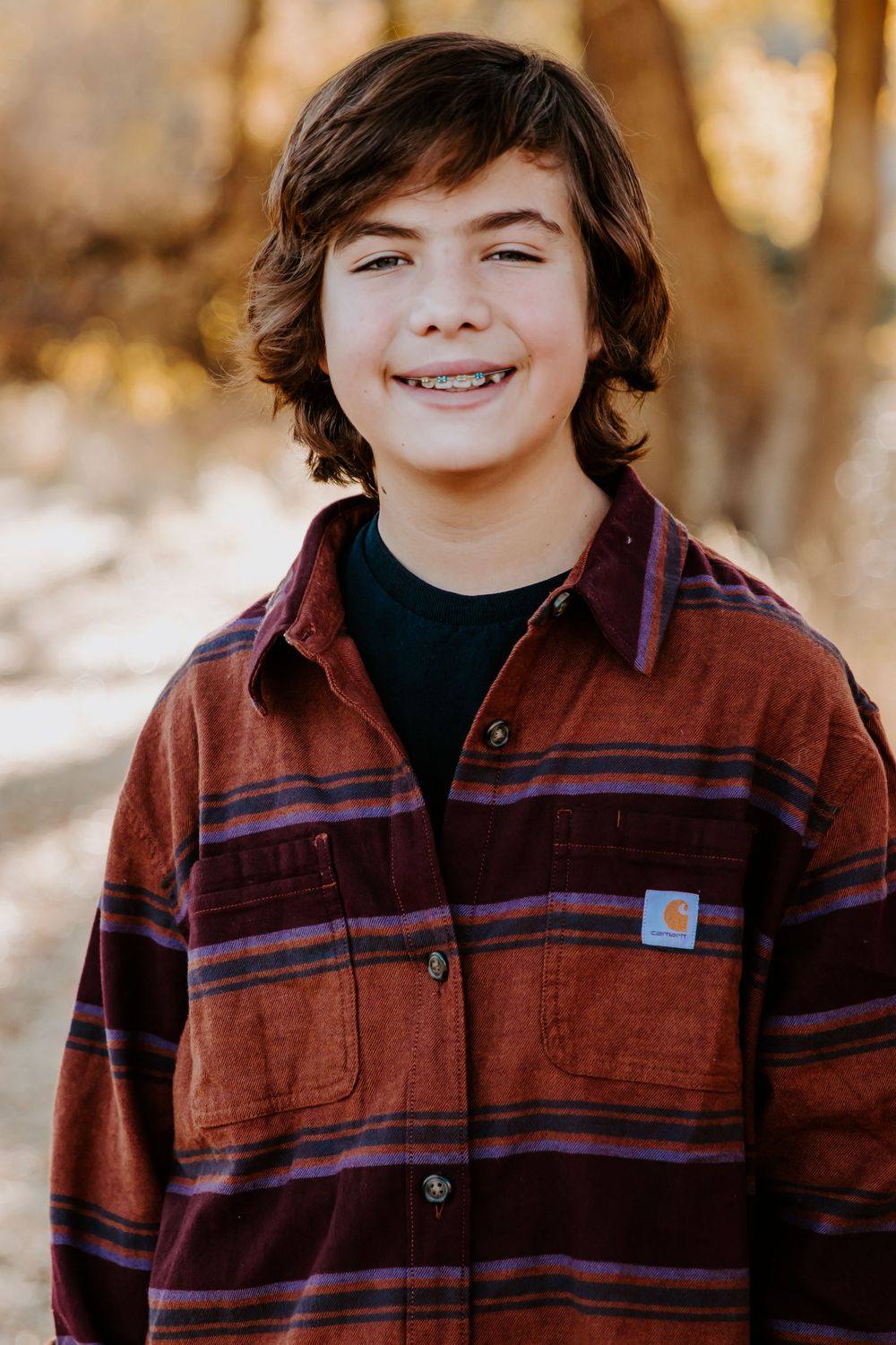 Young teen wearing a striped flannel shirt smiles at the camera outdoors.
