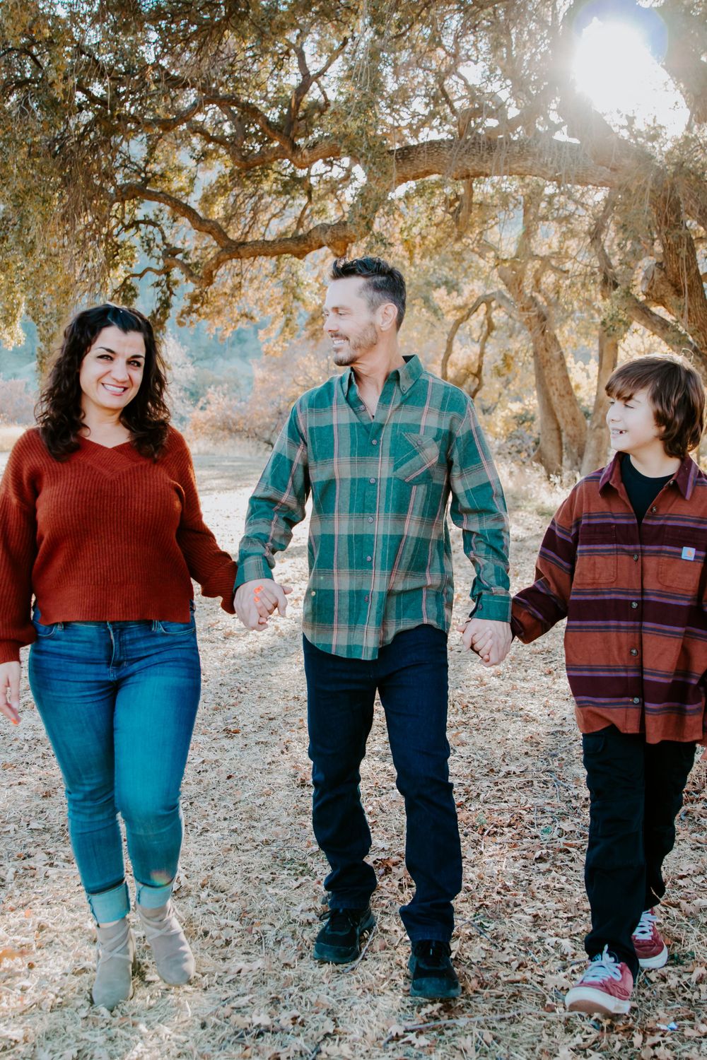 Family of three walking together on a nature trail during golden hour.