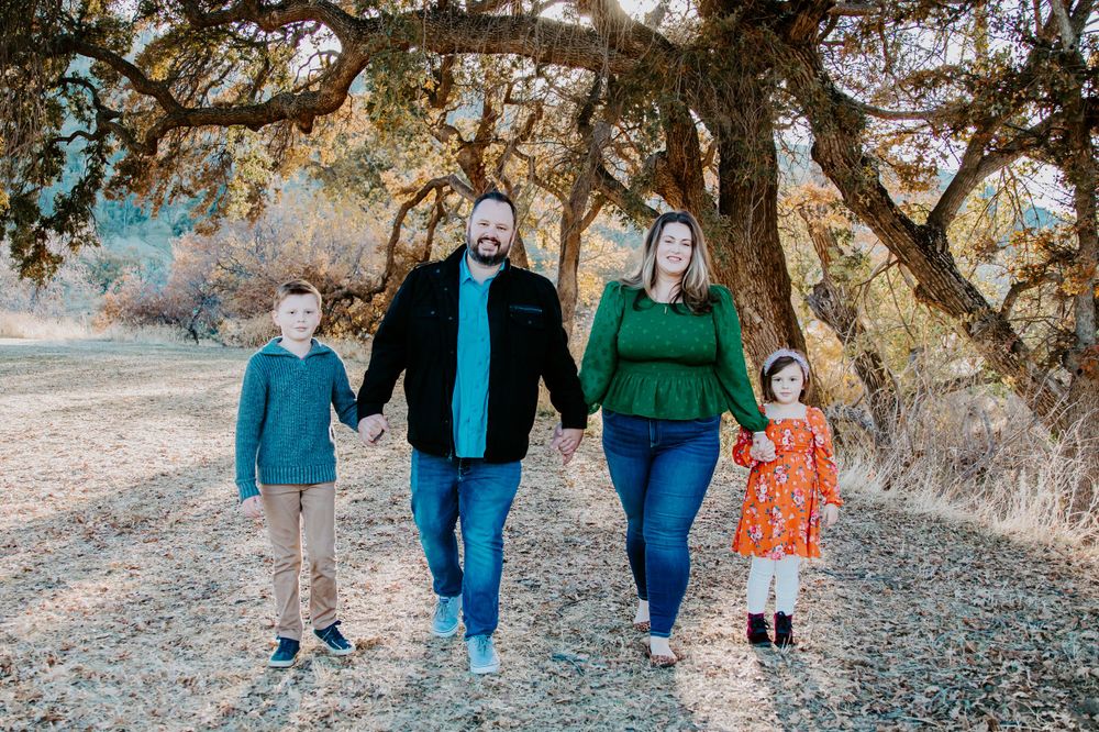 A family of four walking together on a path under oak trees during golden hour.