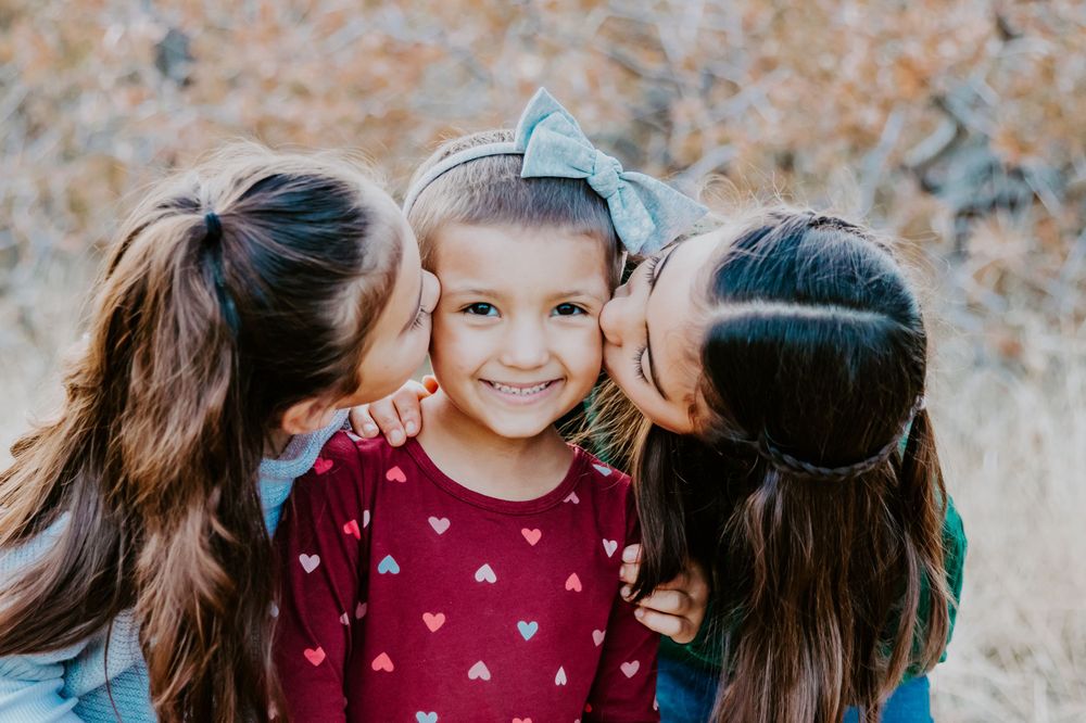 Three children sharing a sweet moment with kisses on the cheek outdoors.