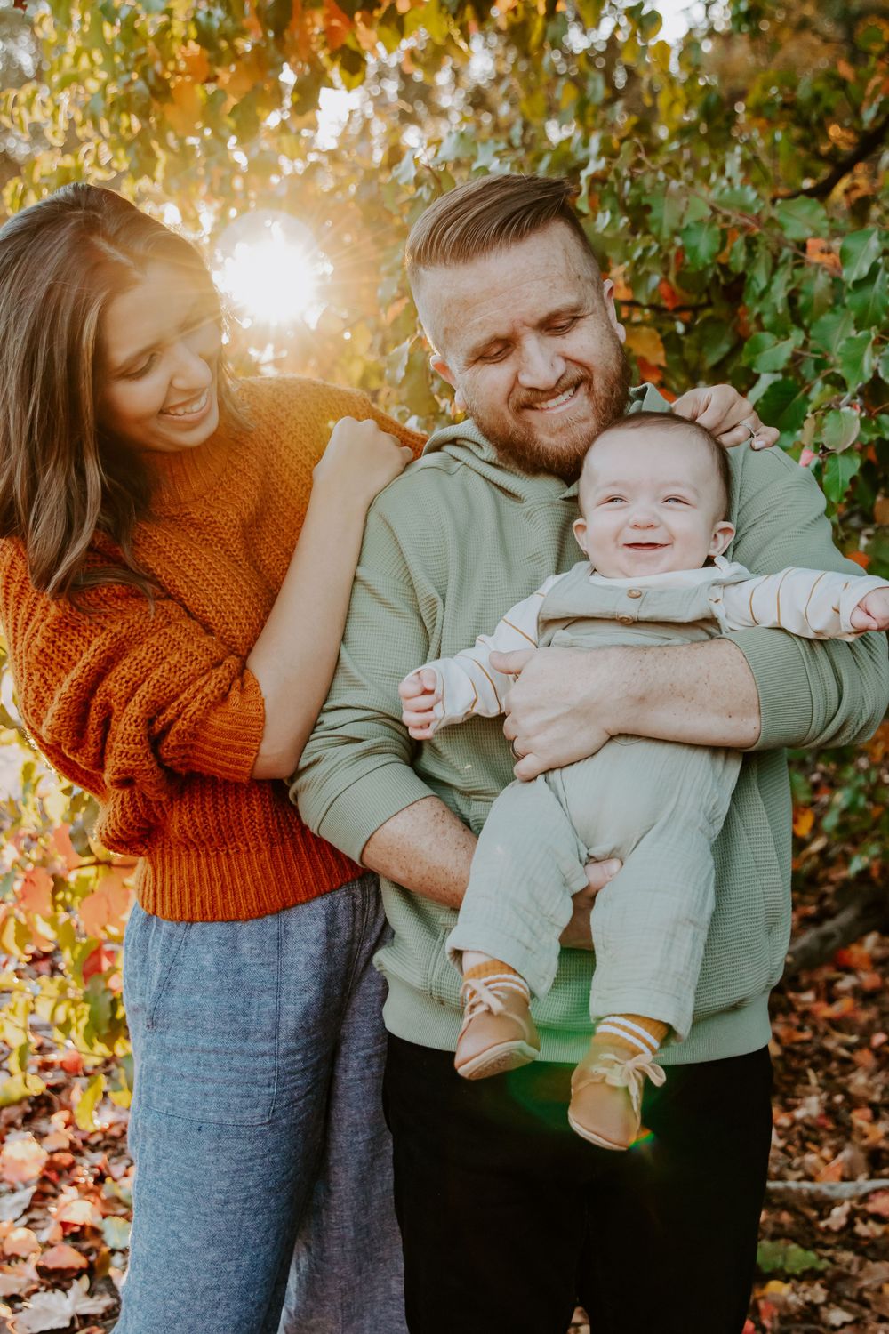 A family poses together outdoors during golden hour autumn sunlight among colorful fall foliage.