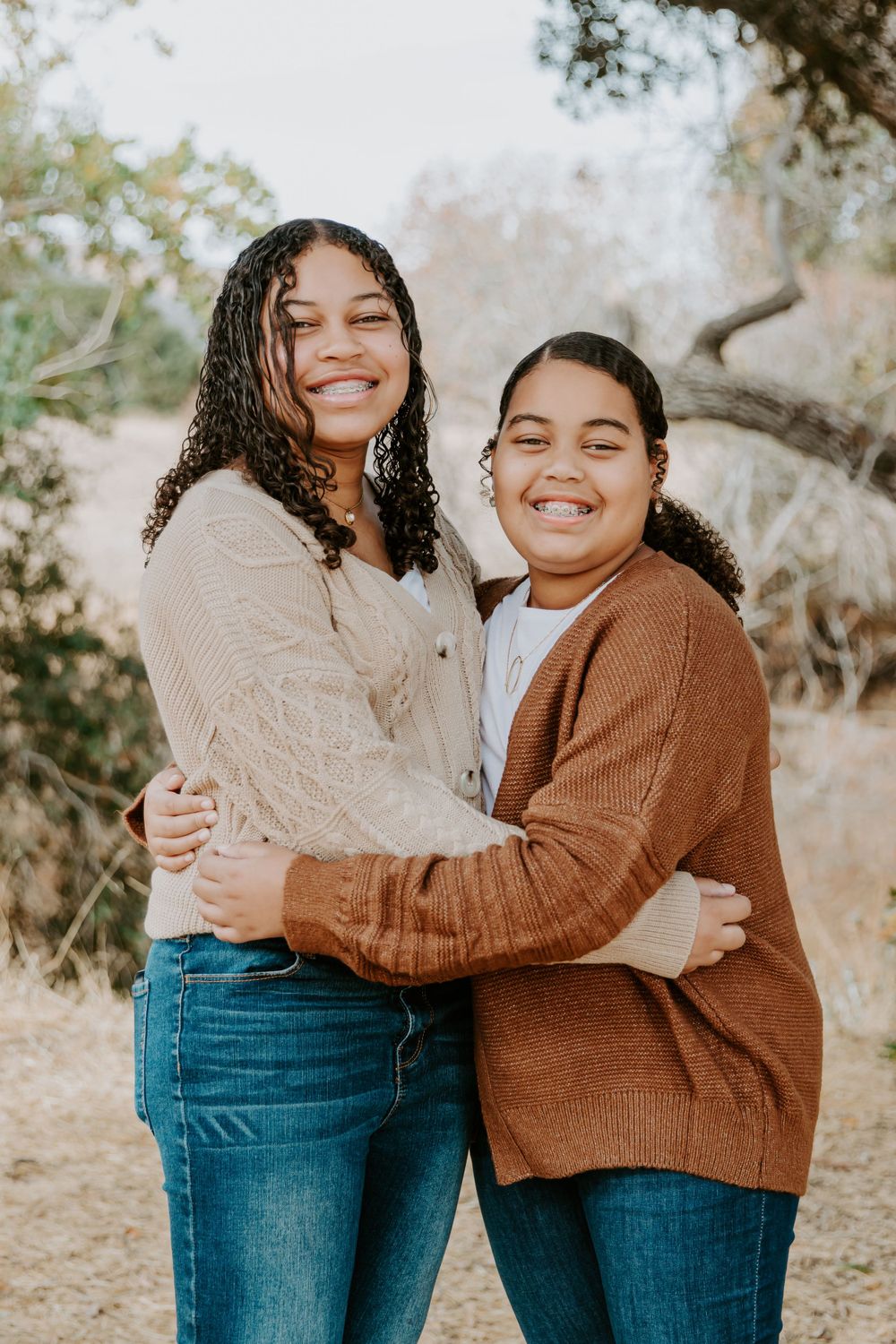 Two people sharing a warm embrace and laughing together while wearing casual sweaters outdoors.