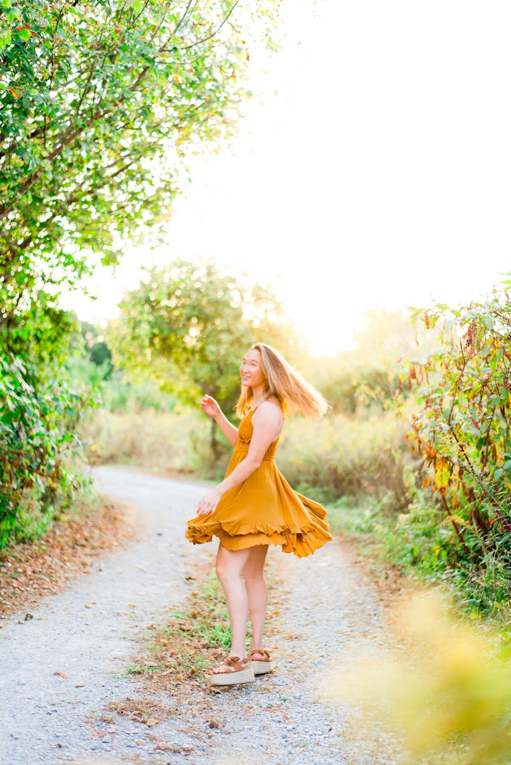 young woman in yellow Adella dress spinning around on a gravel path