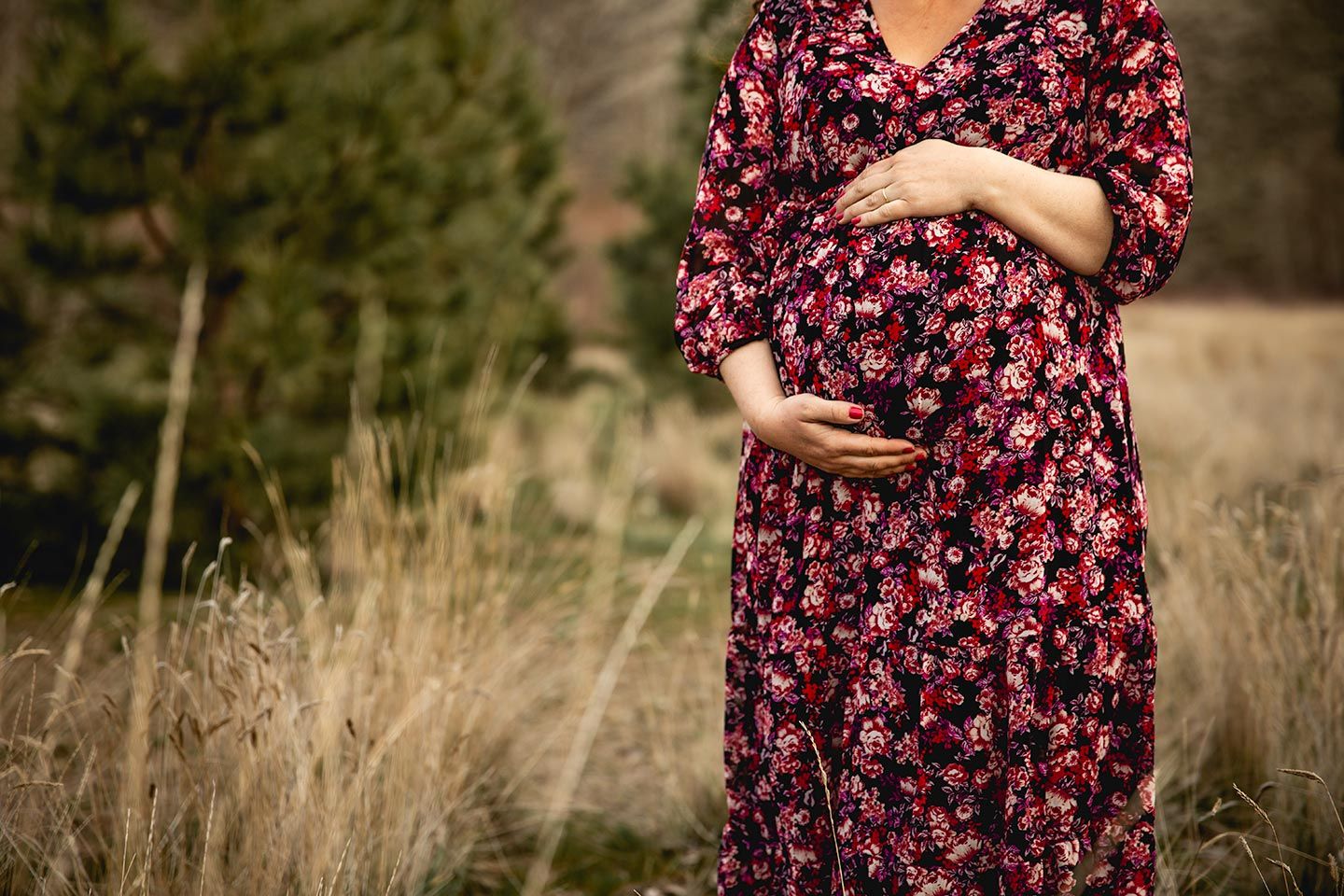 expecting mother holding her round tummy as she stands in a grassy field