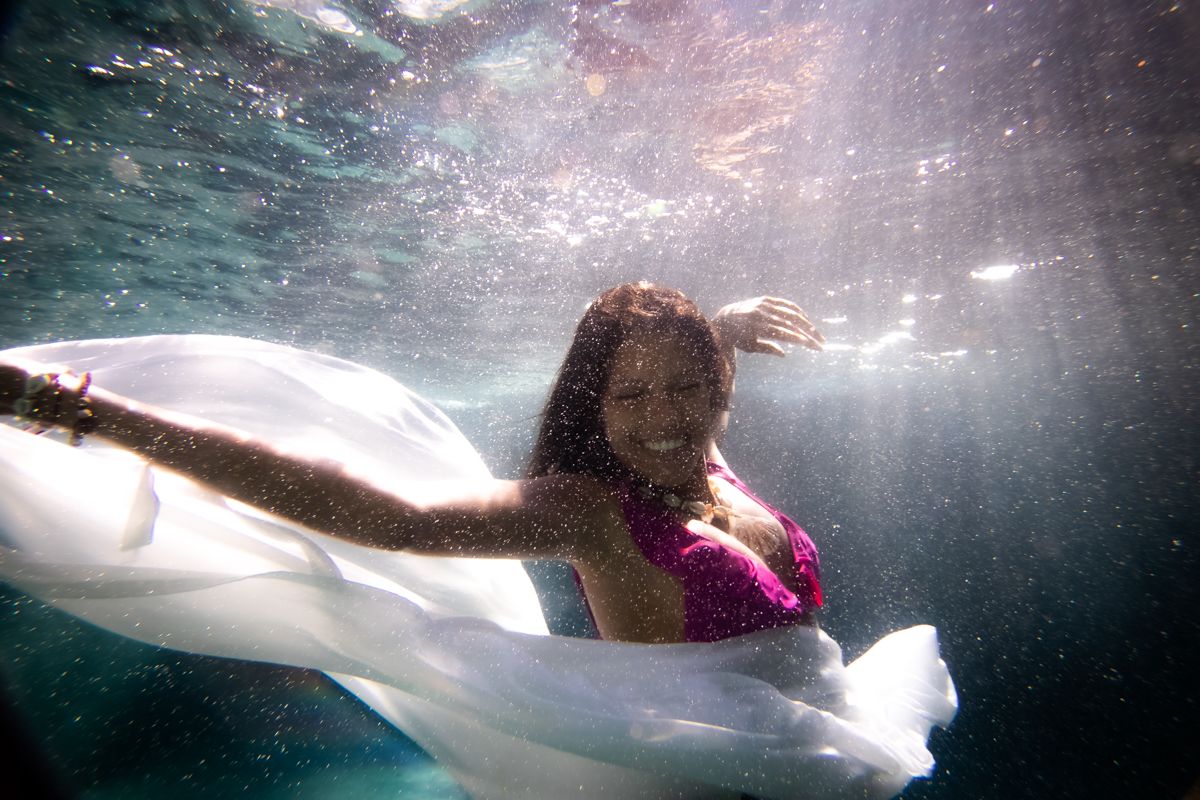 A woman smiling underwater and holding her white floating skirt