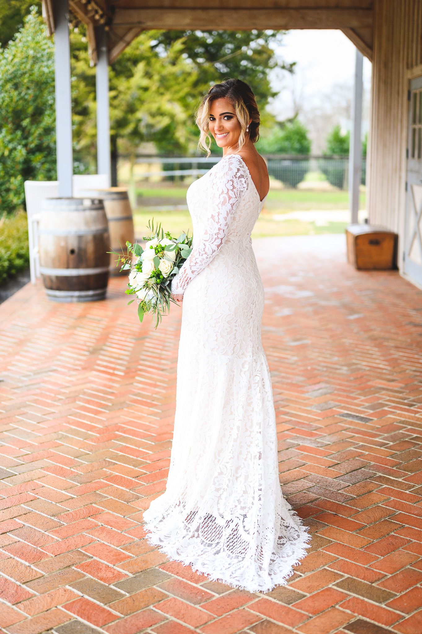 bride holding her bouquet and smiling on barnyard floor at Edel Haus alpaca farm
