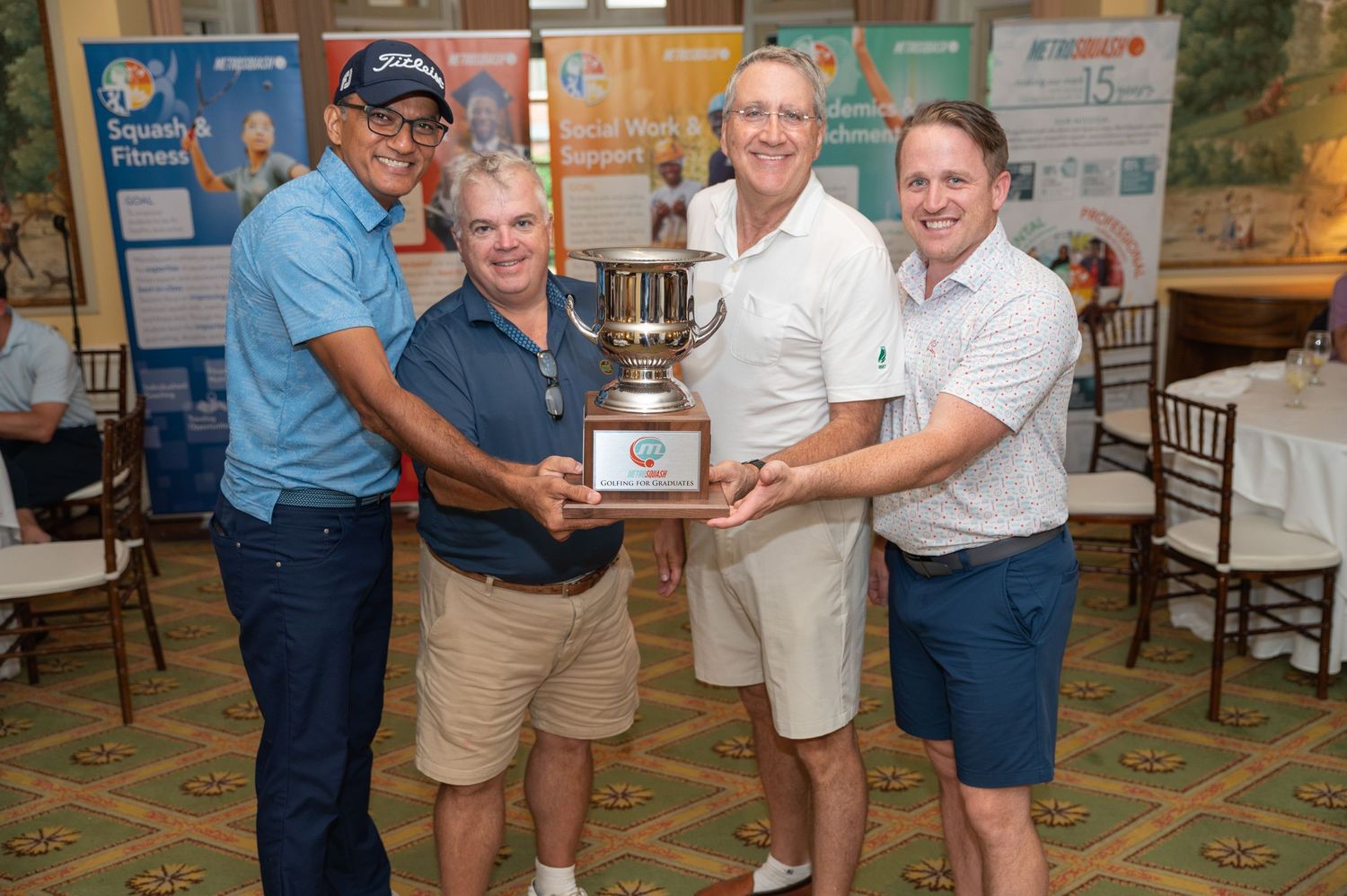 Four people holding trophy together at indoor award ceremony.