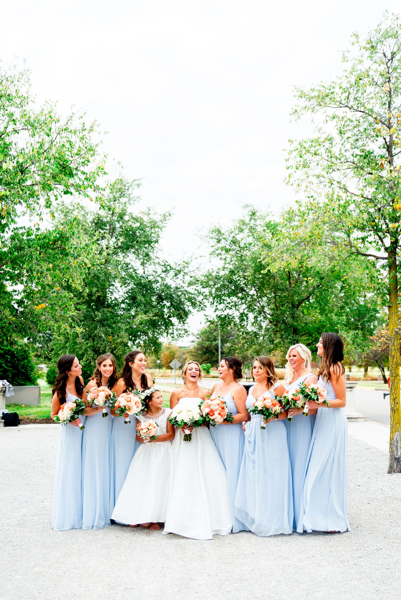 bride laughs with bridesmaids in light blue dresses and coral bouquets at STL Forest Park fall wedding\