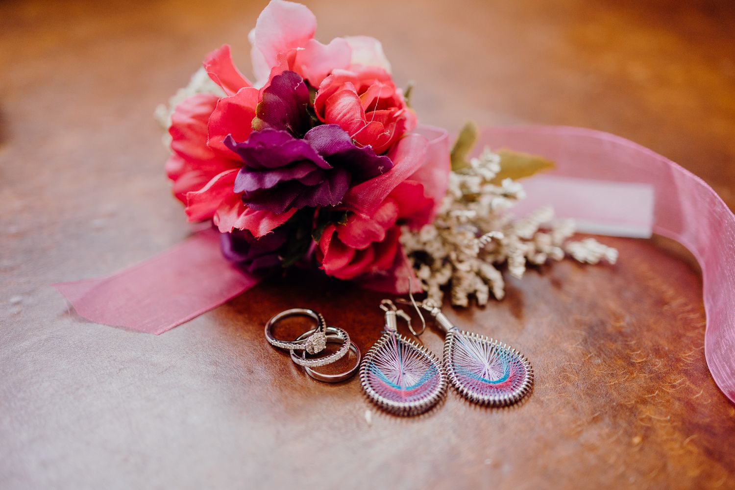 Wedding rings nestled among vibrant pink and burgundy flowers with a pink ribbon.