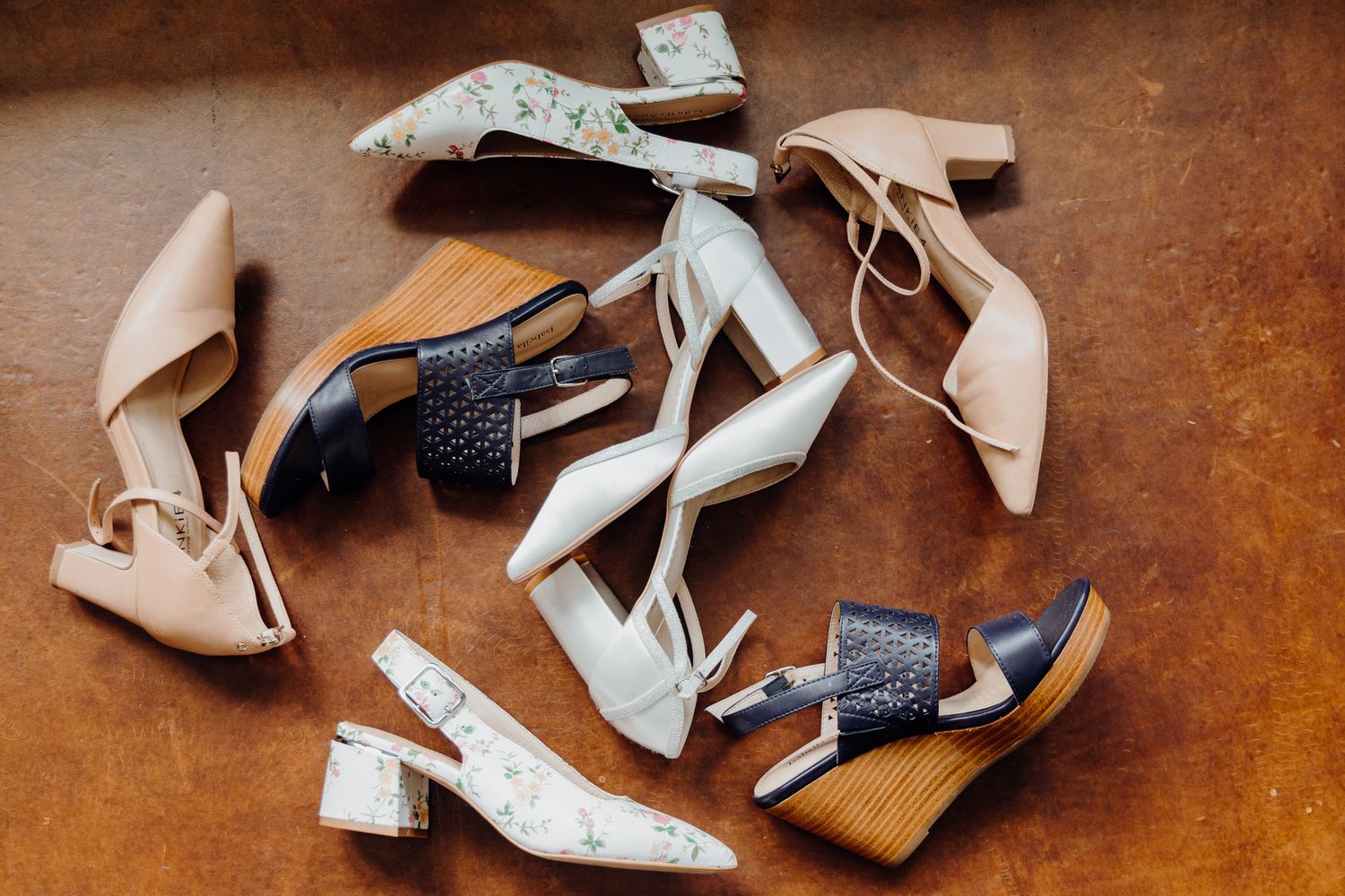 Collection of elegant wedding shoes in neutral tones scattered on a wooden surface.