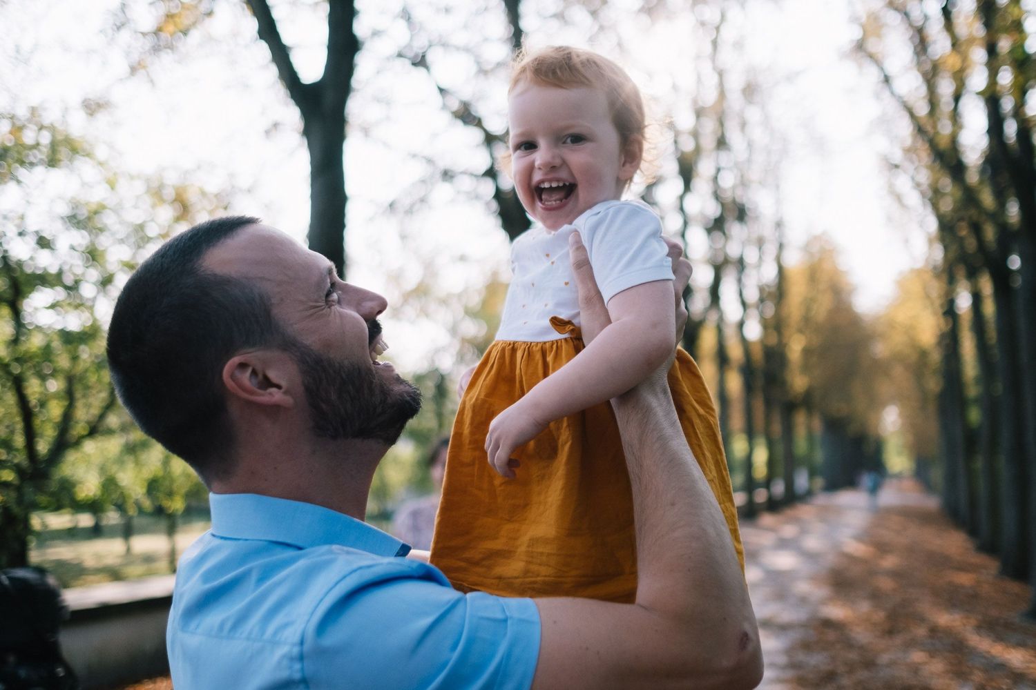Mädchen mit orangefarbenem Kleid wird von Vater hochgehoben