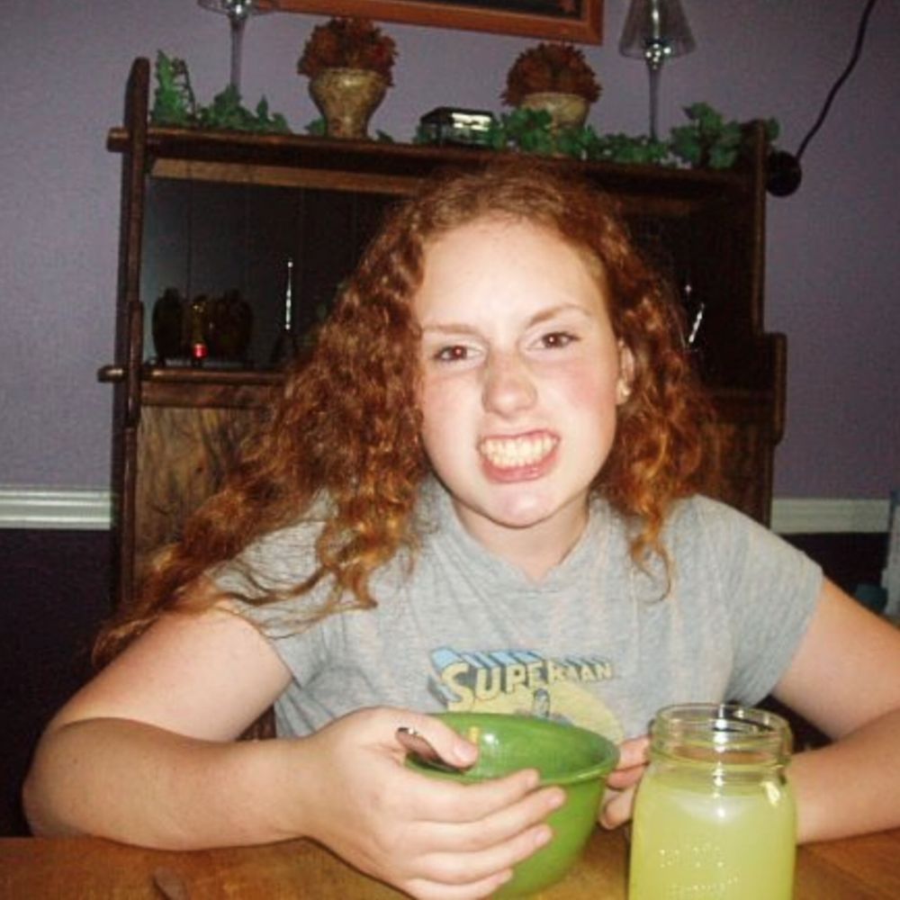 A young Elise Odom around 14 or 15 years old eating a bowl of cereal and making a weird face