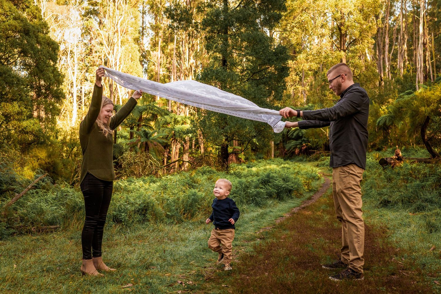 Parents holding a white parachute as their toddler runs under it