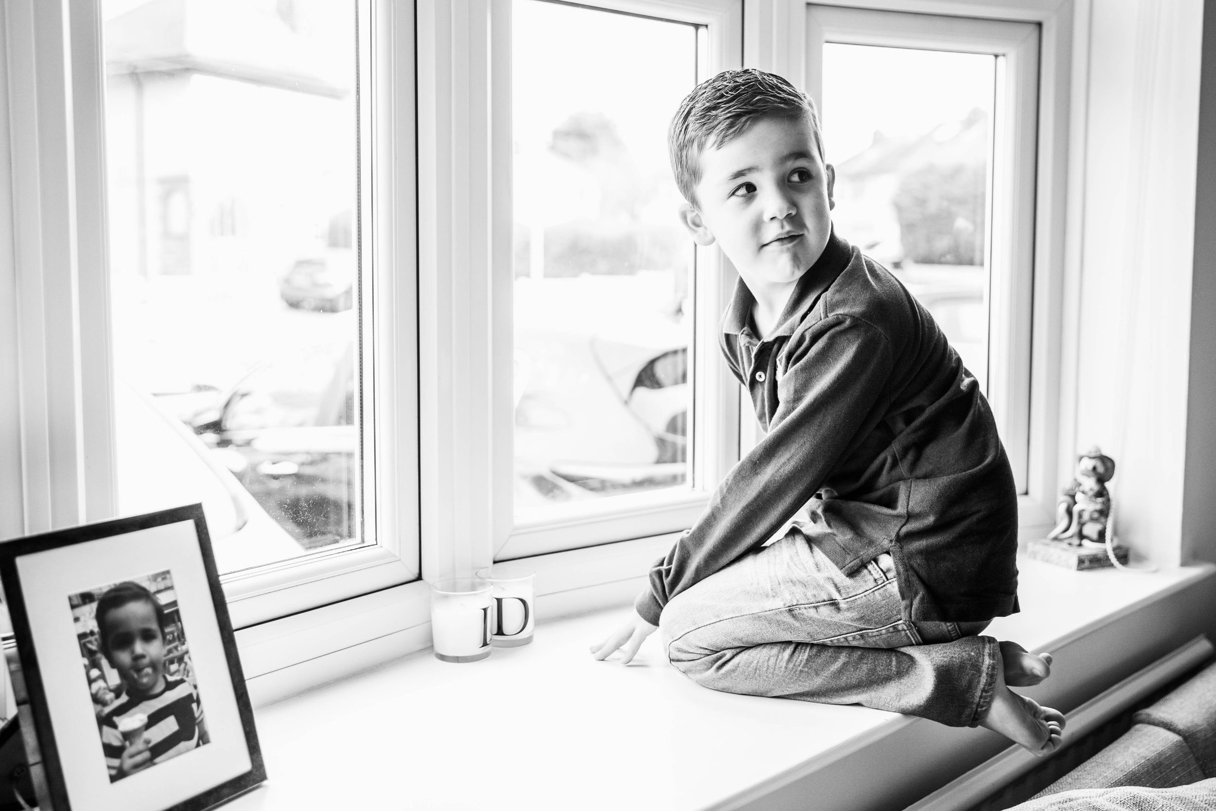 black and white portrait of boy sitting on windowsill