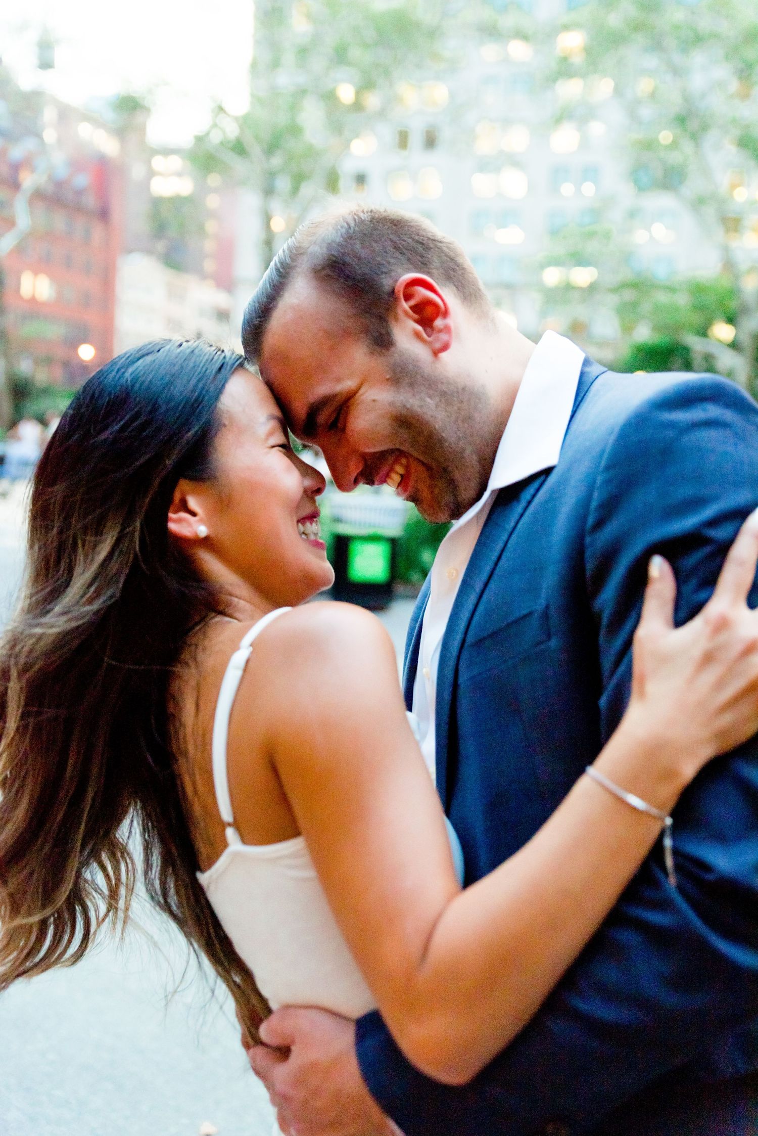 man and woman laughing with foreheads together in front of building at dusk in Madison Square Park NYC