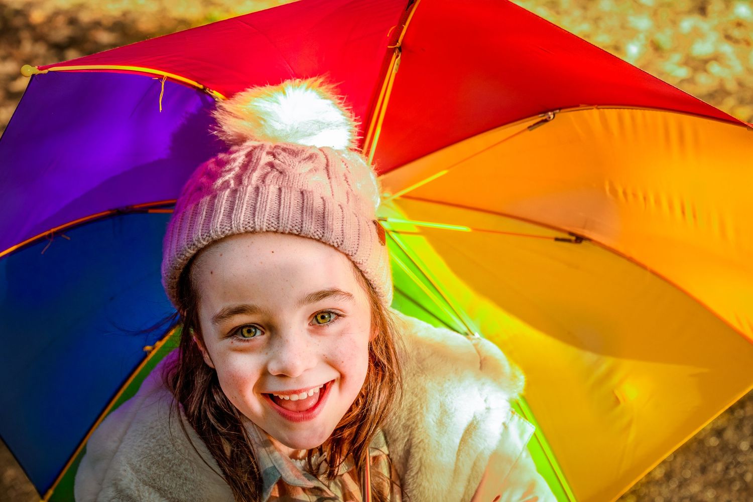 Smiling girl below a rainbow umbrellas