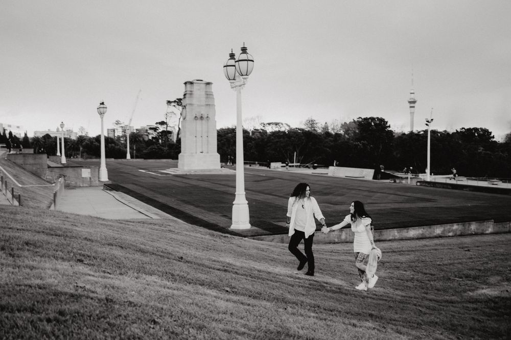 Black and white photo of a couple walking down a hill near historic architecture.