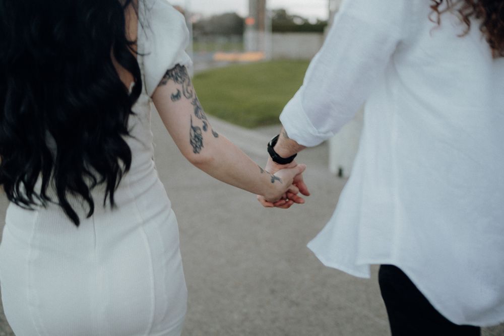 Close-up of tattooed arms and joined hands in white outfits.