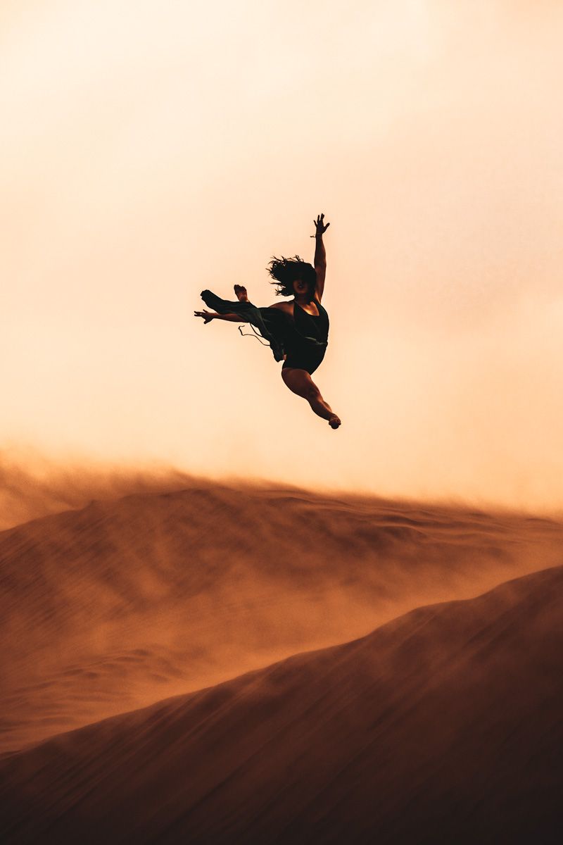 ballerina leaping high in the air during a windstorm at the sand dunes
