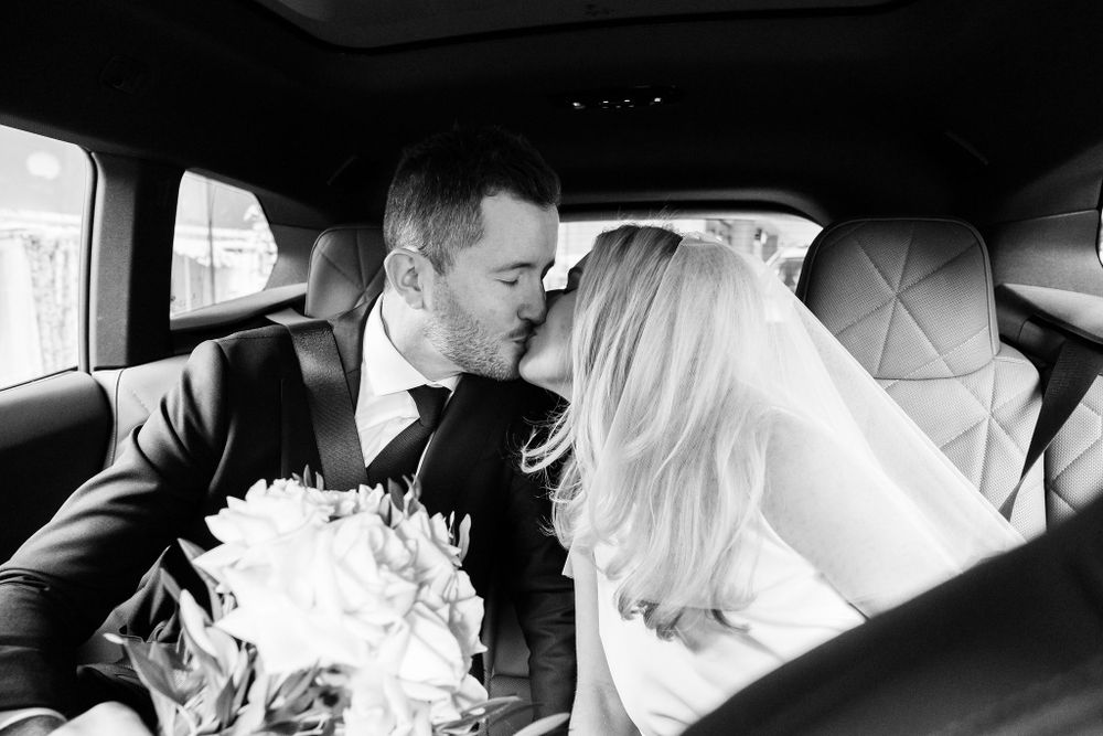 Intimate black and white moment of newlyweds in car backseat.